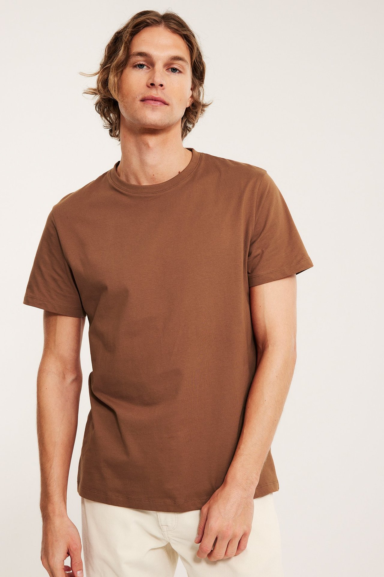 Frontbilde av en mann i brun kortermet T-skjorte i bomull og lysebeige bukser.