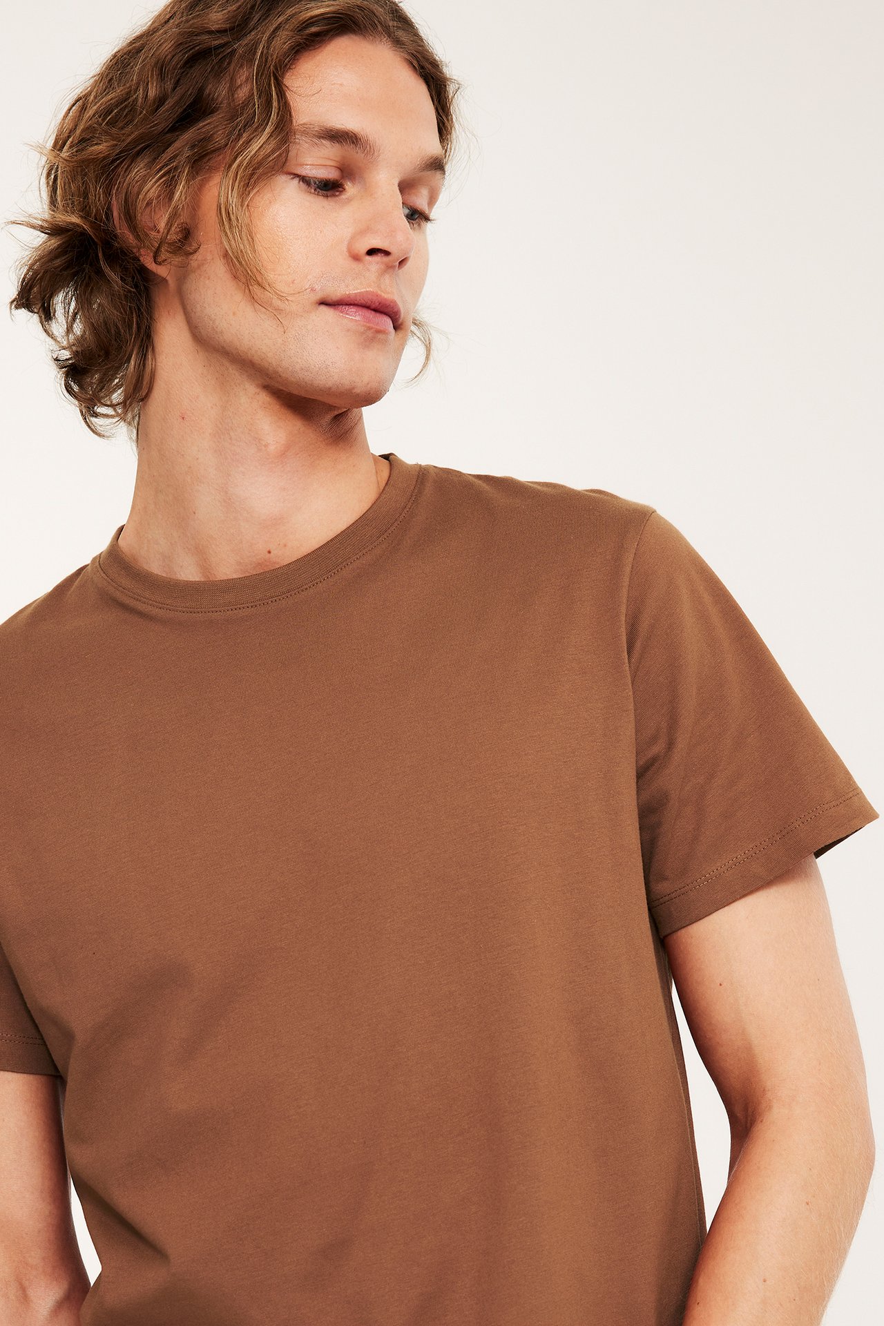 Lähikuva miehestä yllään ruskea yksivärinen puuvillainen pyöreäkauluksinen t-paita, edestä ja sivulta.