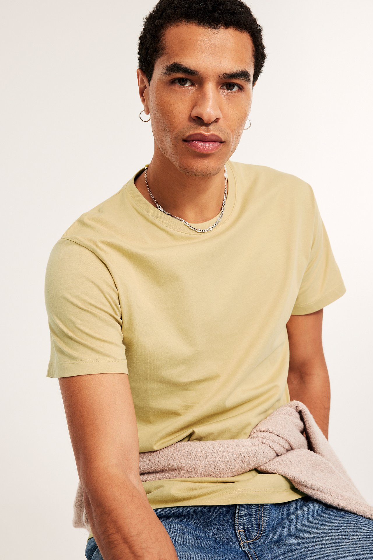 Widok z przodu: Mężczyzna w jasnym żółtym t-shircie, niebieskich dżinsach i swetrze zawiązanym w pasie.