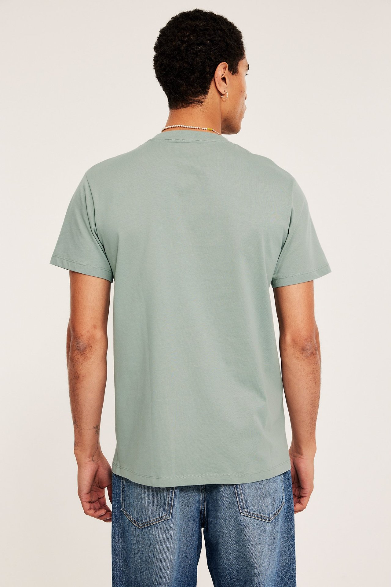 Widok z tyłu: mężczyzna w jasnozielonej bawełnianej koszulce, niebieskich dżinsach i naszyjniku z koralików.