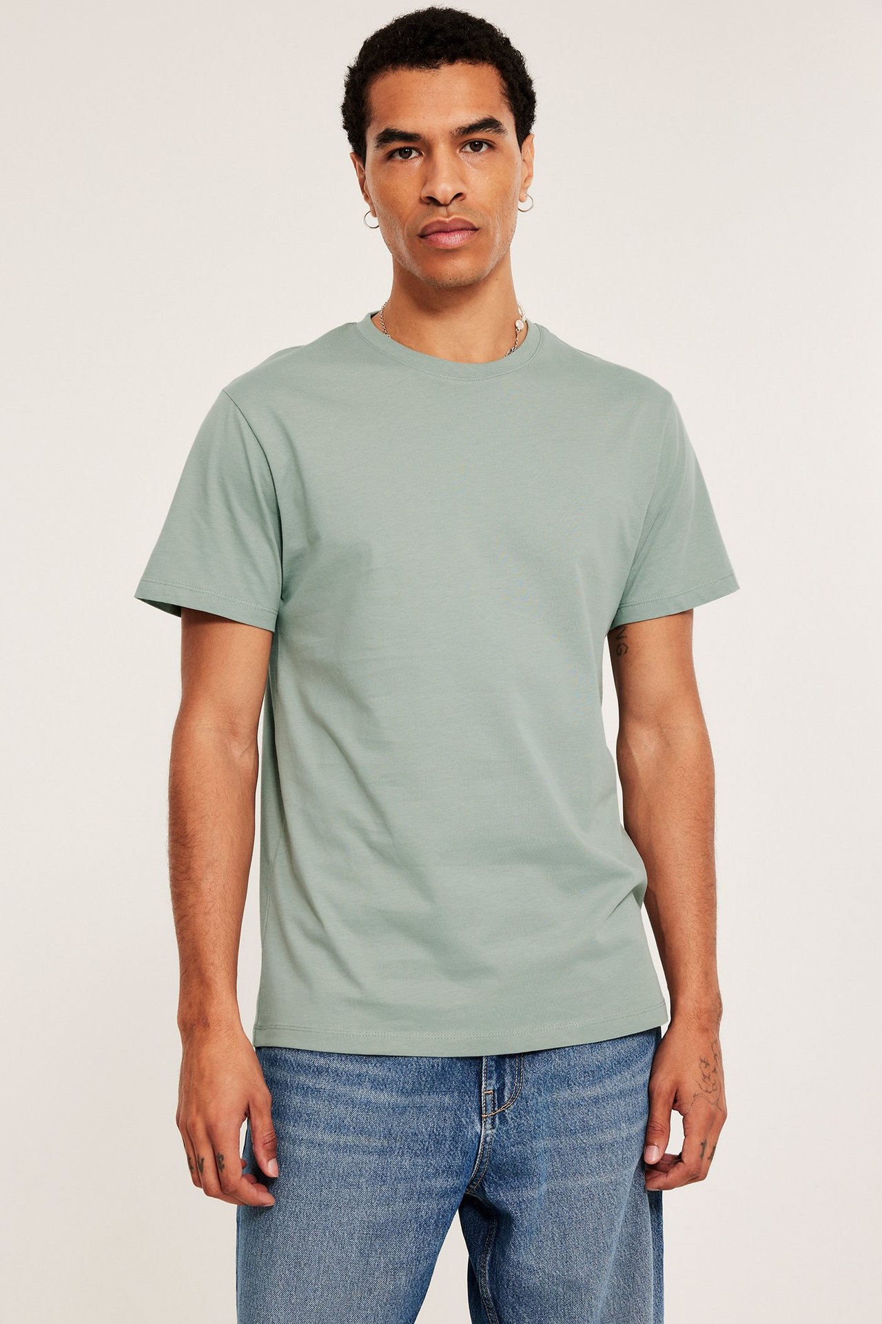 Edestäpäin mies yllään vaaleanvihreä pyöreäkauluksinen t-paita ja siniset farkut.