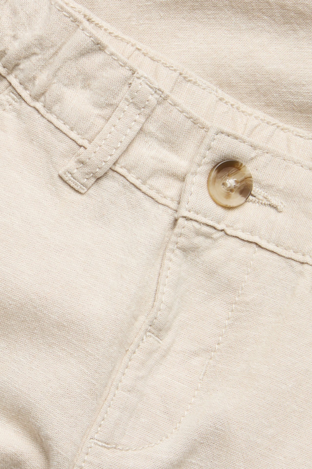 Zbliżenie na jasnobeżowe spodnie z mieszanki lnu z brązowym guzikiem i szlufkami.
