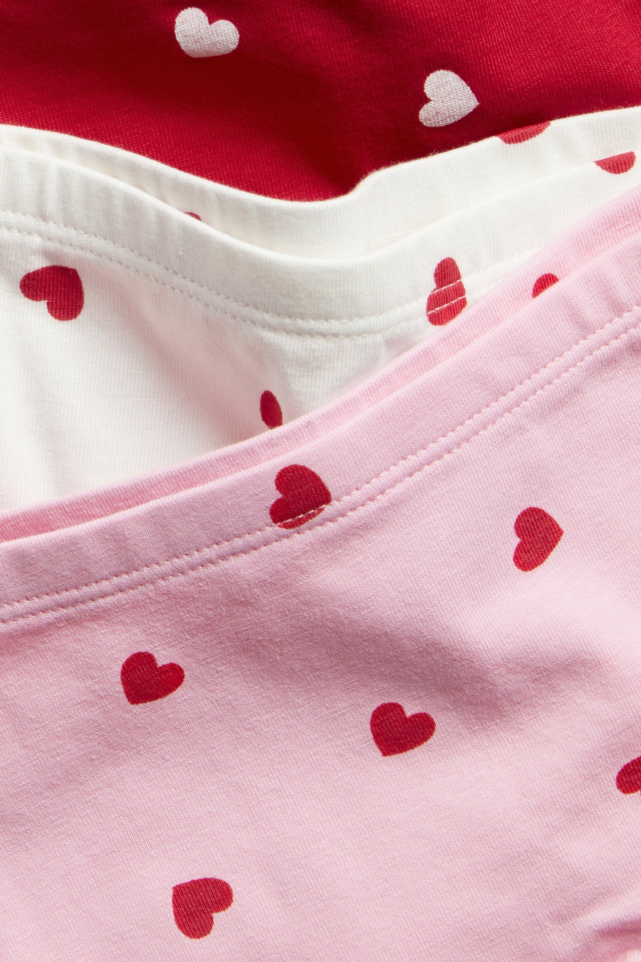 Zbliżenie trzech dziecięcych bokserek we wzór serca w kolorach ecru, różowym i czerwonym.