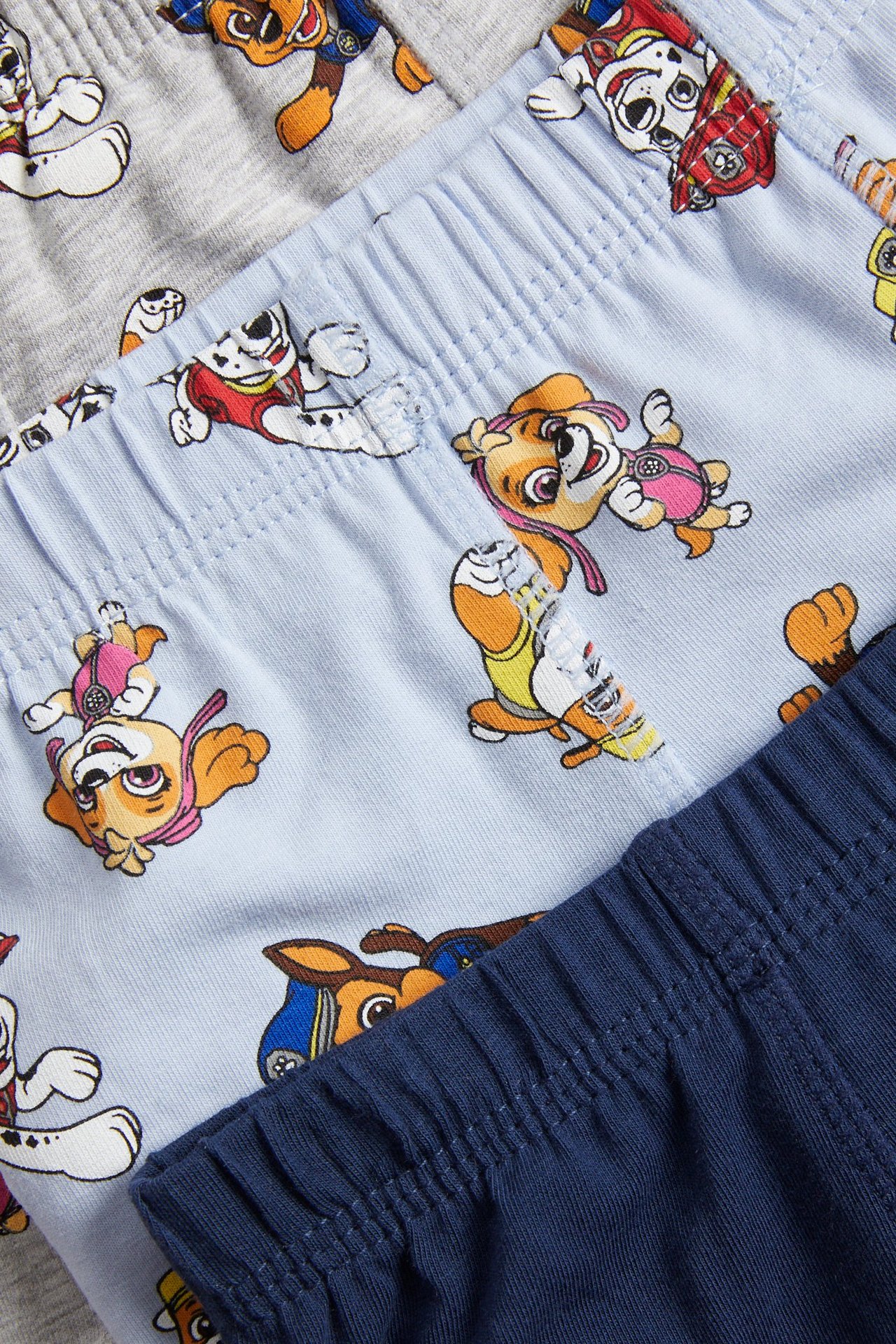 Lähikuva vaaleansinisistä lasten boksereista Paw Patrol -painatuksella, harmaiden ja tummansinisten parien kanssa.