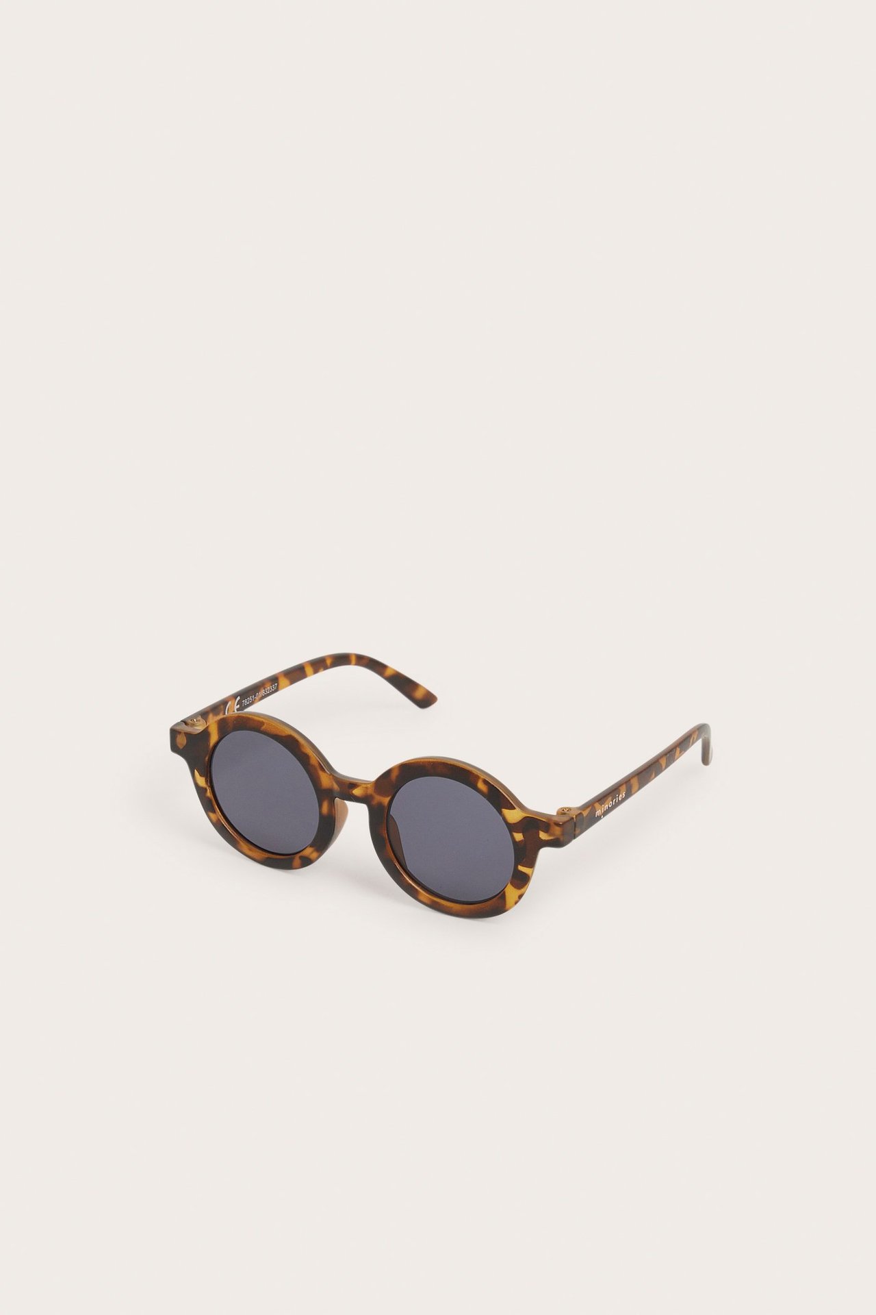 Sidestilt bilde av runde, mønstrede brune plastsunglass til baby med mørke glass.