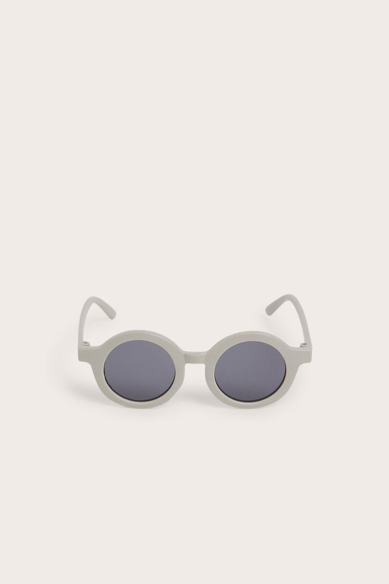 Frontvisning av baby-solbriller i lys beige resirkulert plast med mørke ovale glass.