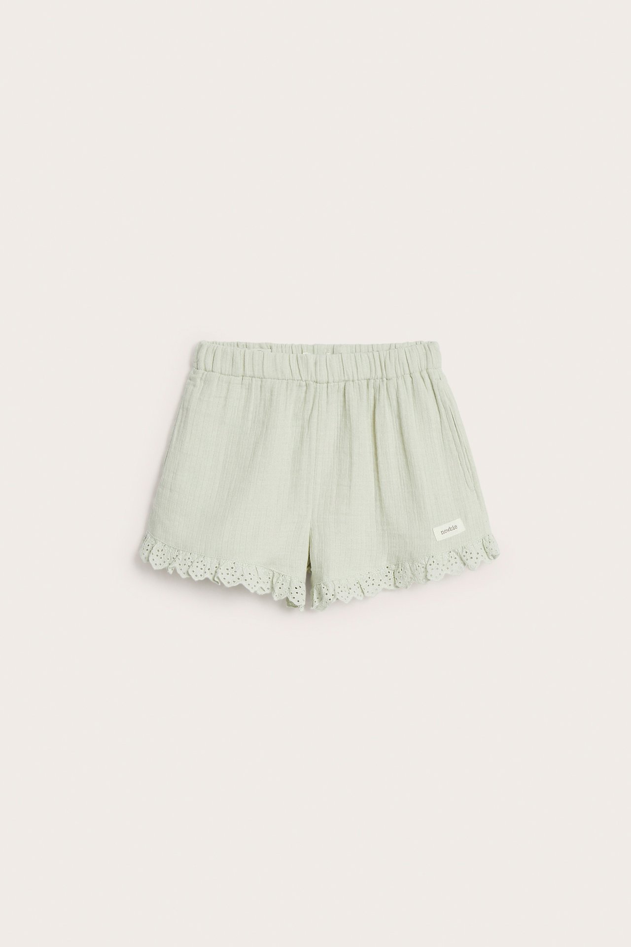 Frontvy av ljusgröna vävda bomullsshorts med resårlinning och spetsvolang i bensluten.