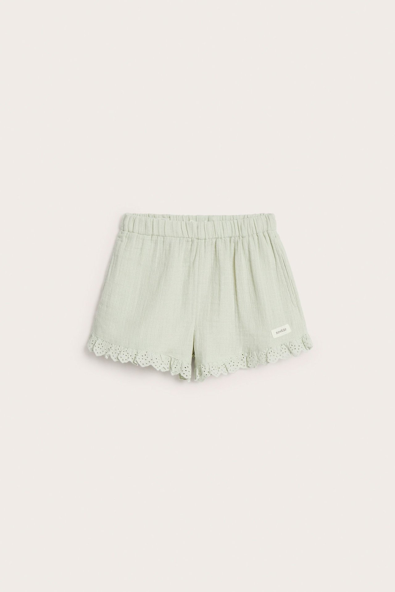 Widok z przodu jasnych zielonych bawełnianych szortów z elastycznym pasem i koronkową falbanką.