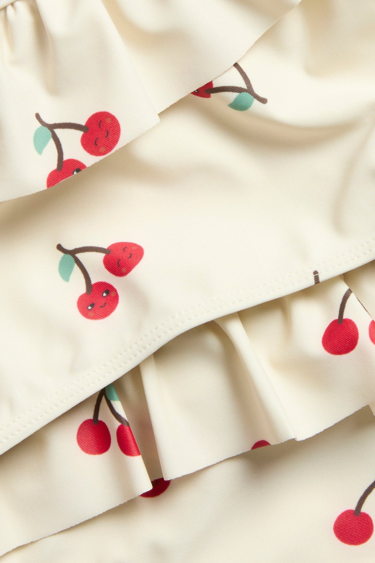 Lähikuva vaaleanbeigestä bikinista, jossa on punainen kirsikkakuvio ja röyhelöyksityiskohtia.