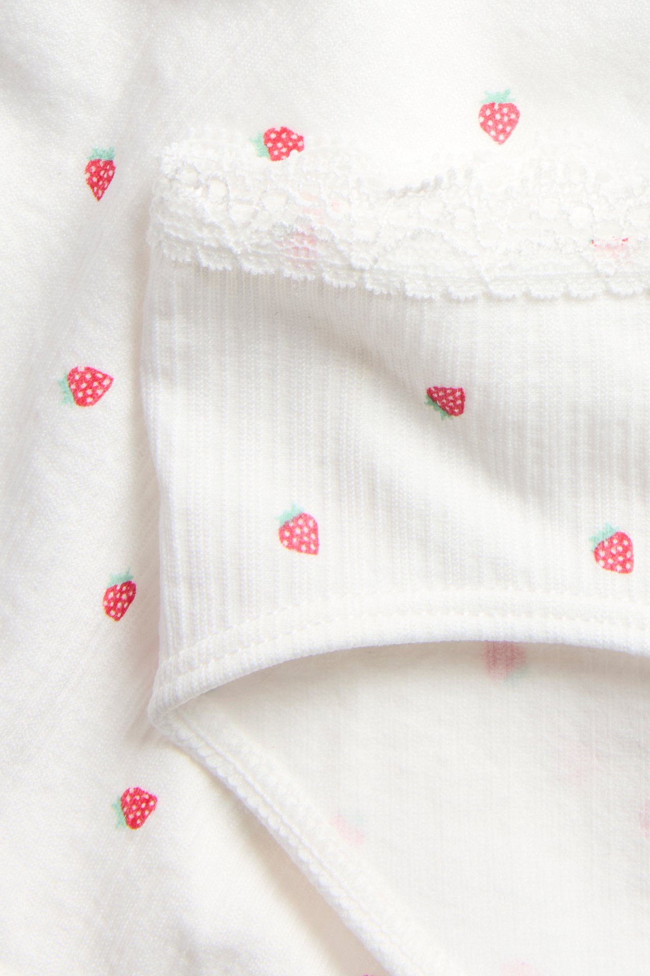Zbliżenie na off-white bezszwowe figi dziecięce z nadrukiem truskawek i koronkową lamówką.