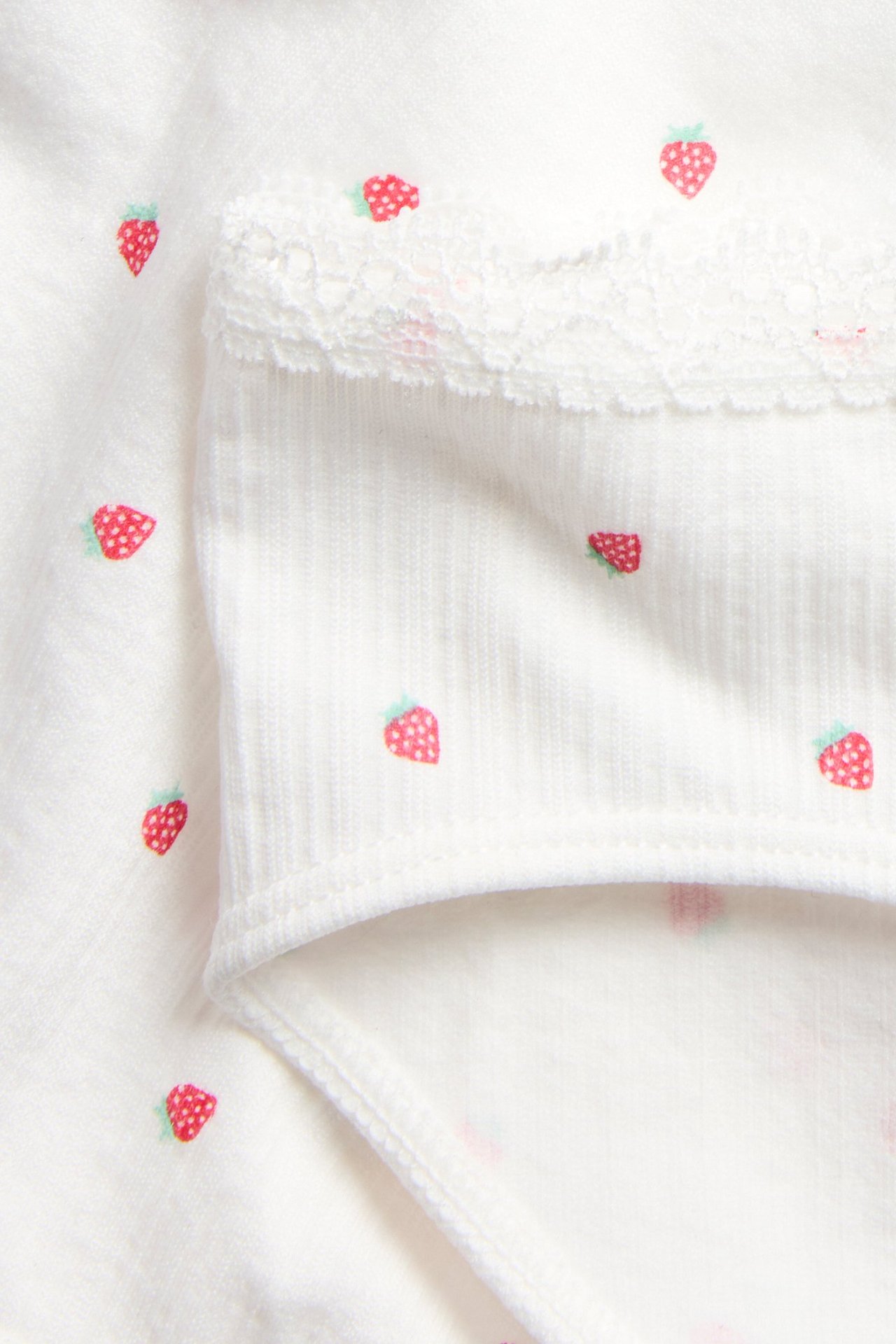 Zbliżenie na off-white bezszwowe figi dziecięce z nadrukiem truskawek i koronkową lamówką.