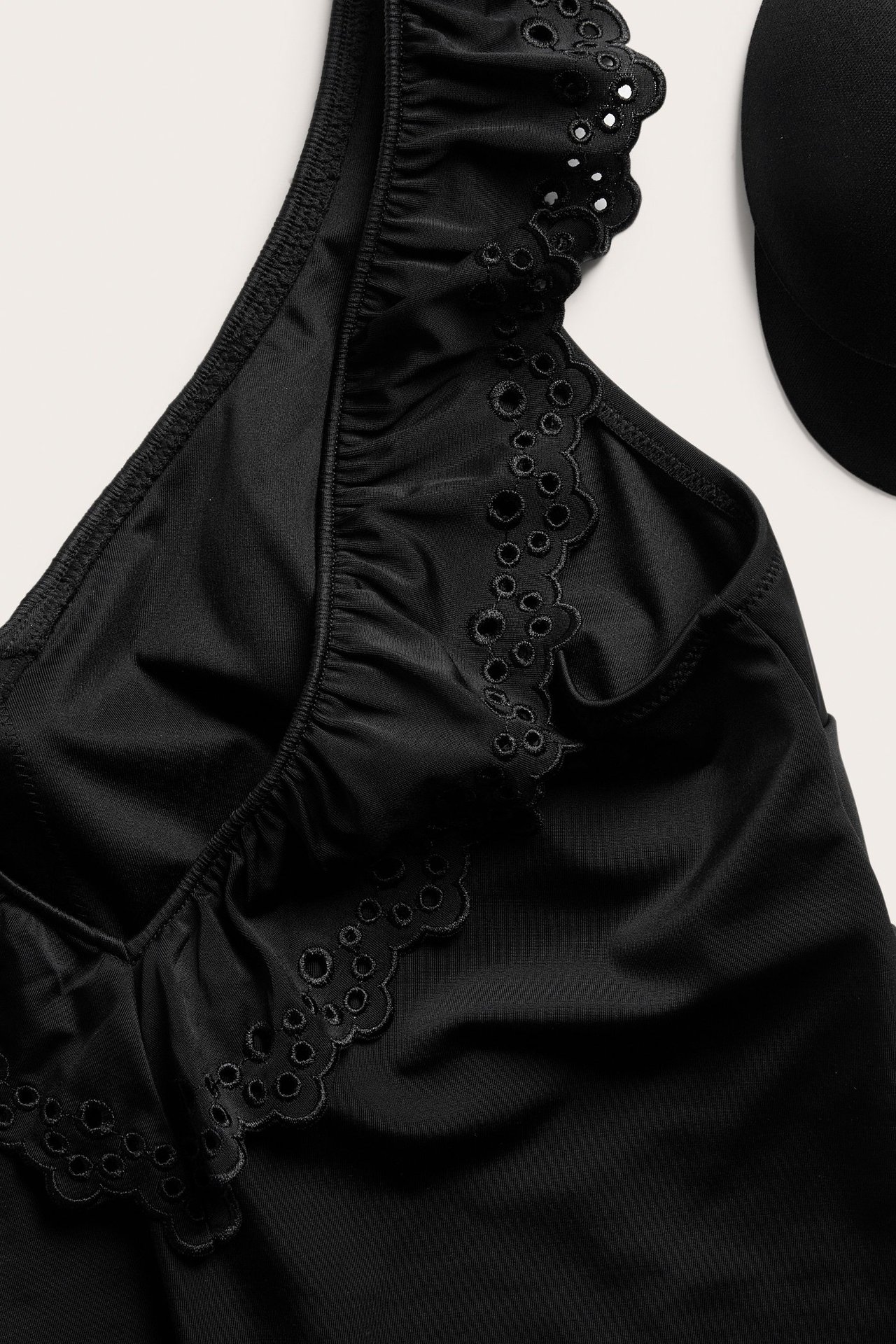 Lähikuva mustasta uimapuvusta, jossa on brodeerattuja reikiä ja röyhelöitä.