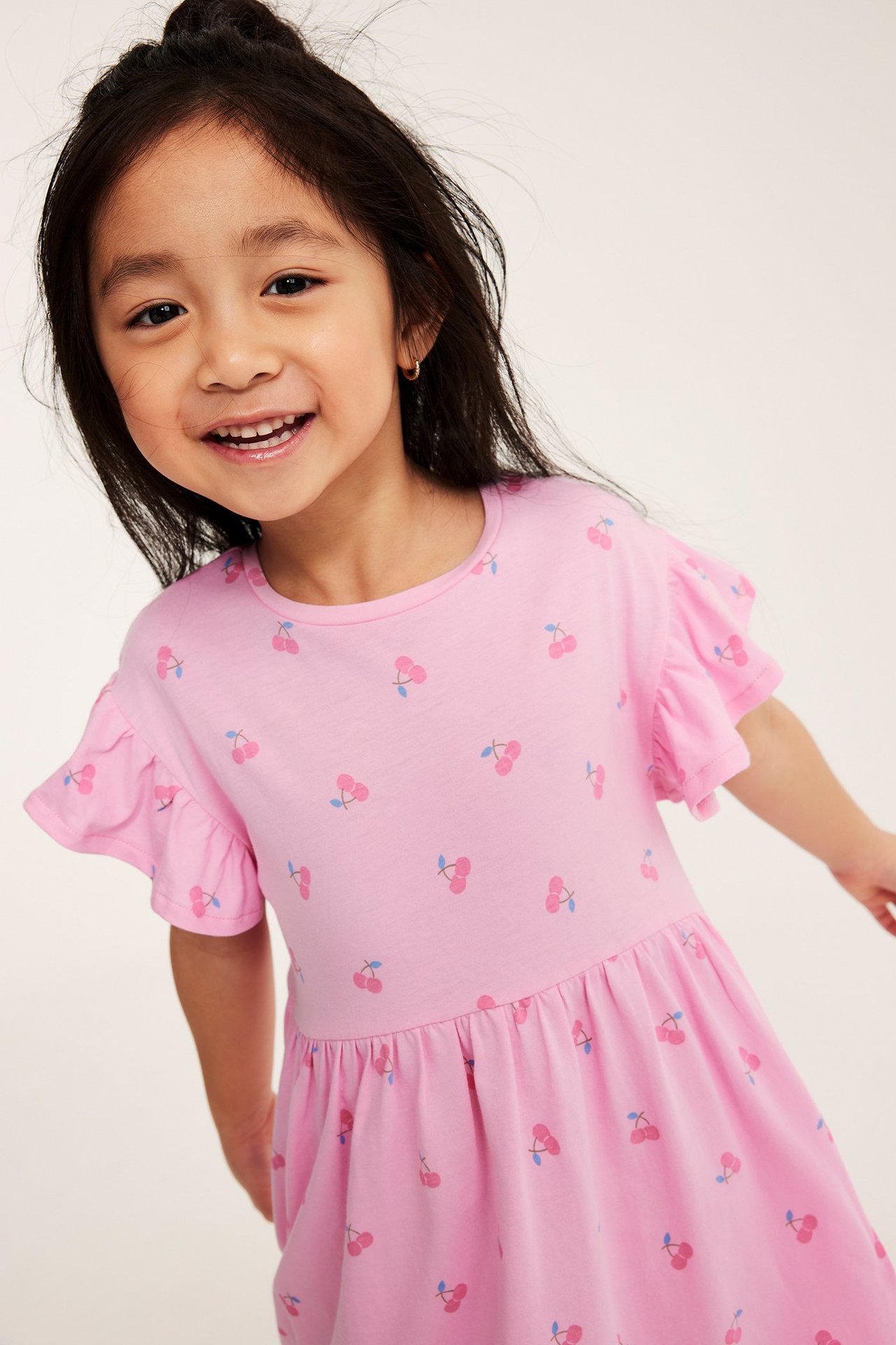 Dziecko w jasnoróżowej bawełnianej sukience z wiśniami i falbankami na rękawach.