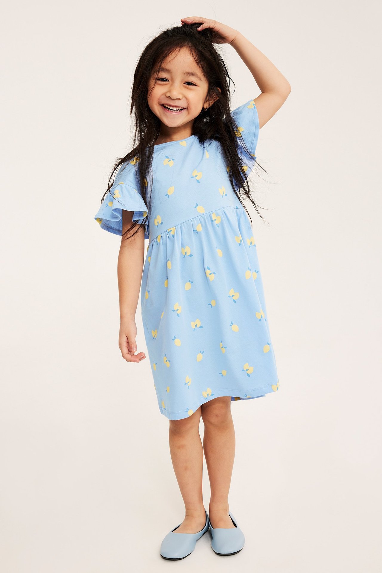 Edestäpäin kuvassa lapsi yllään vaaleansininen sitruunakuvioinen puuvillamekko ja vaaleansiniset ballerinat.