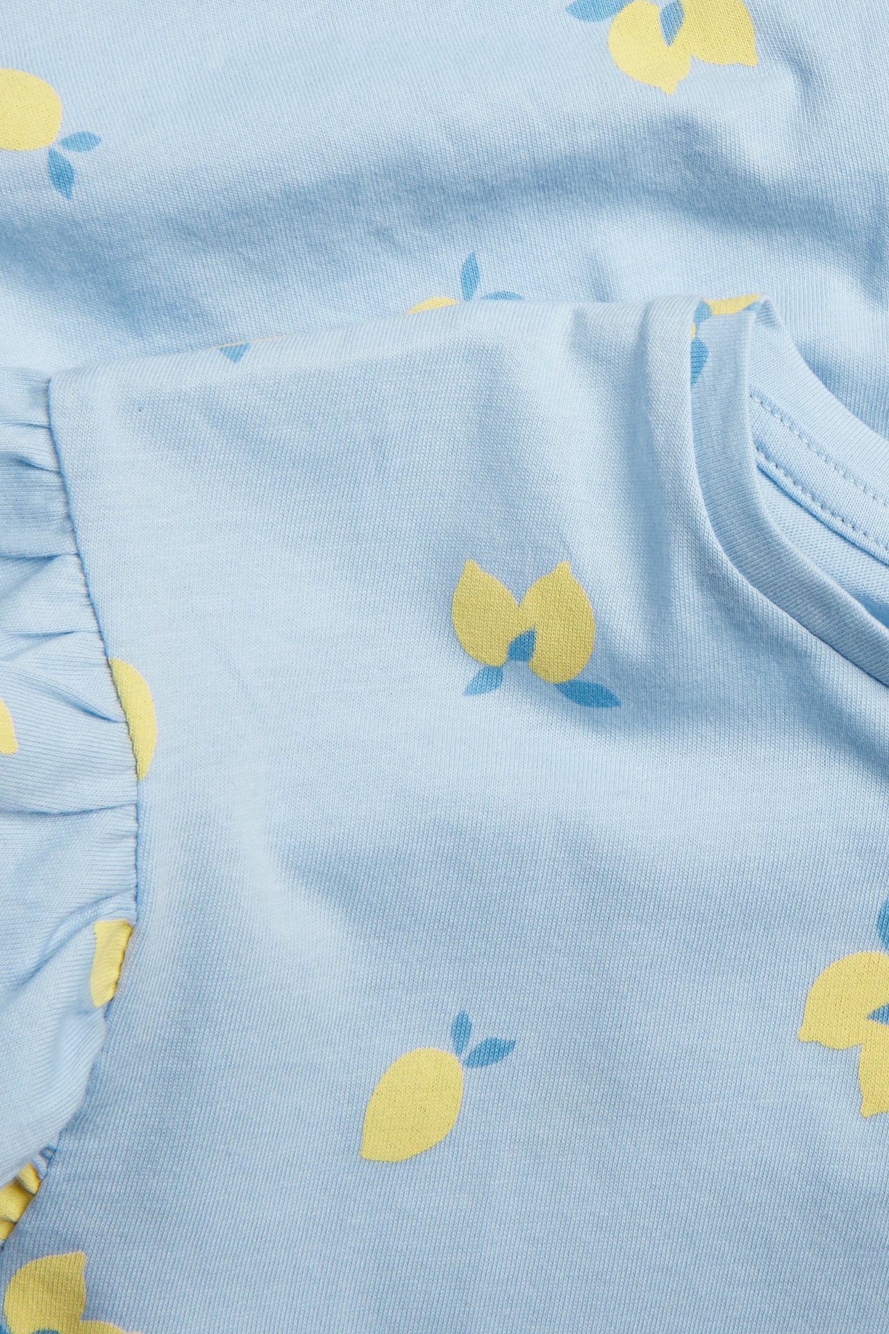 Zbliżenie na jasnoniebieską dziecięcą sukienkę z bawełny, z wzorem cytryn i falbanowym rękawem.