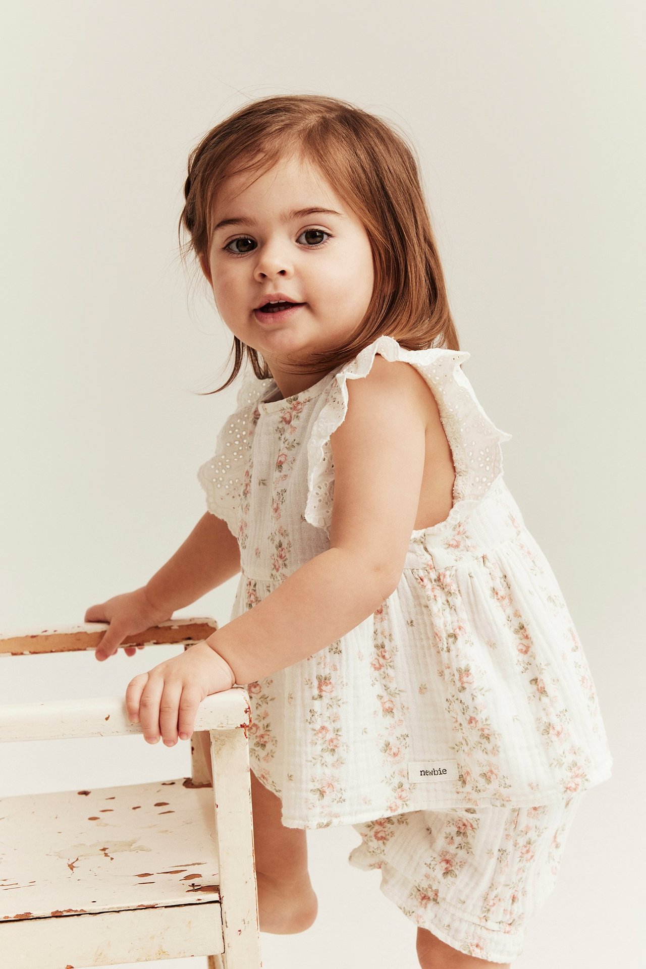 Edestä: Vauva tyttö luonnonvalkoisessa kukkakuvioisessa musliinisetissä, jossa peplum-toppi ja röyhelöhihat.