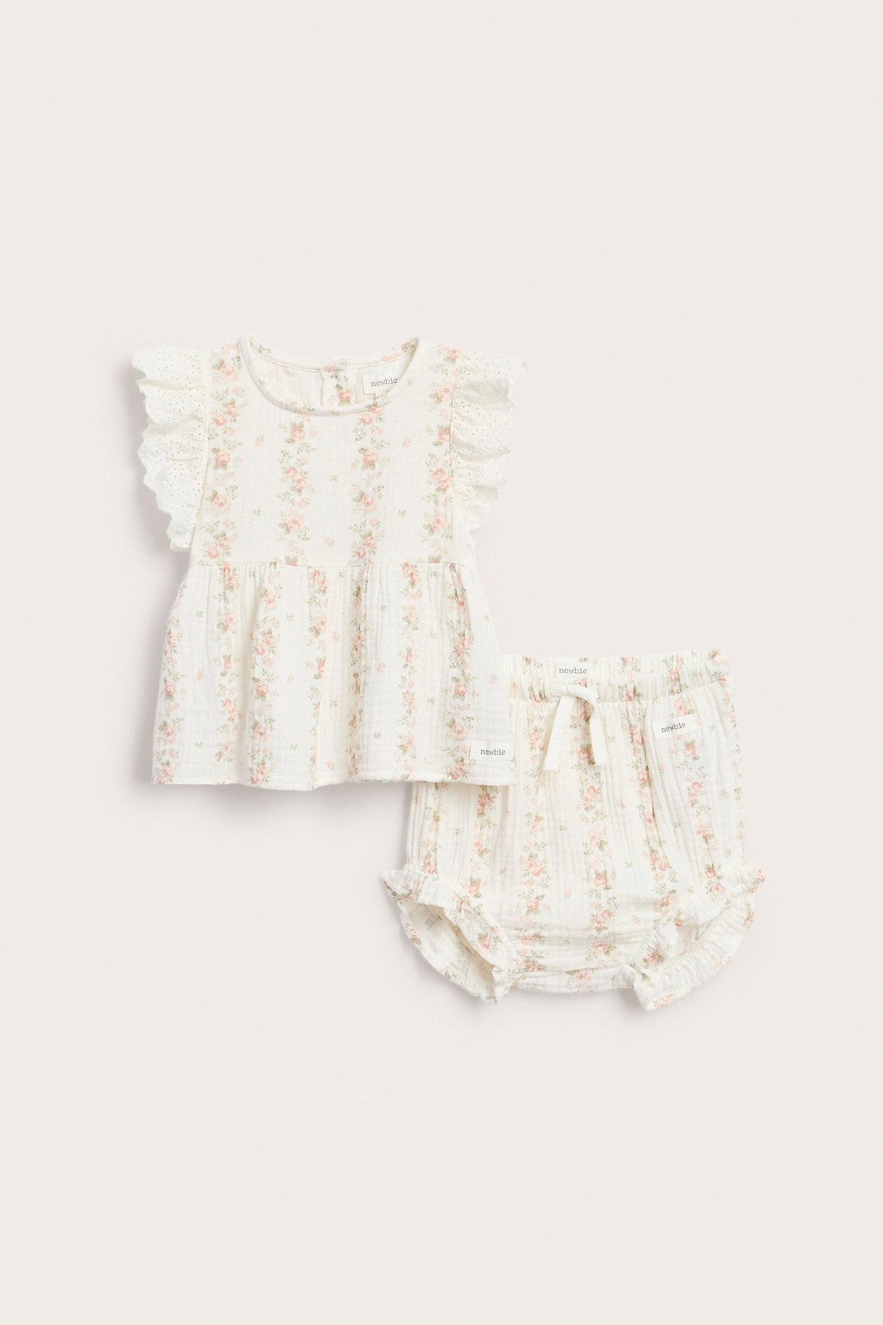 Frontutsikt: Offwhite musselin babypeplumtopp med blomstertrykk, volangermer og matchende shorts.
