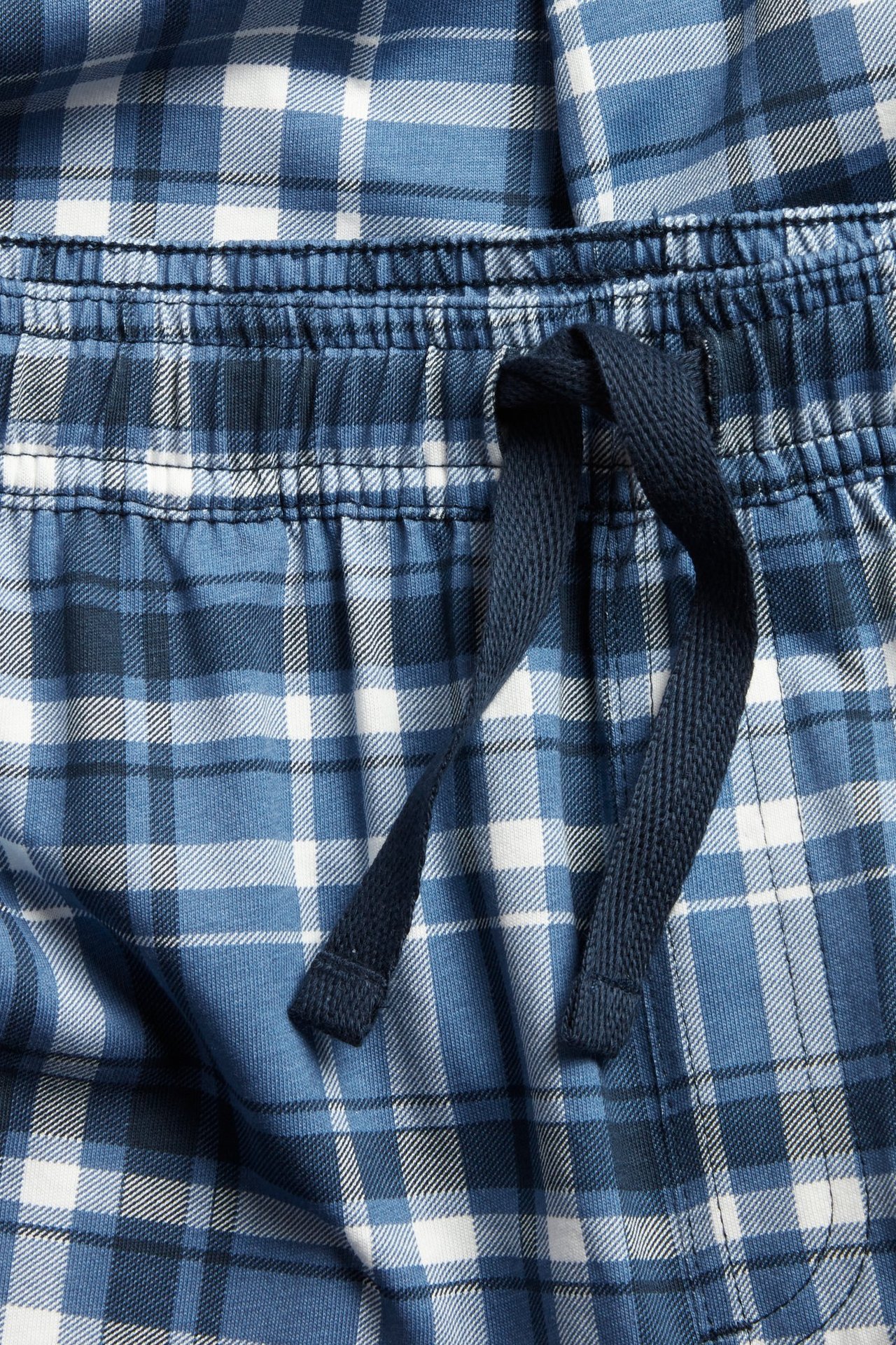 Närbild av blåvitrutiga pyjamasbyxor i jersey med resårlinning och mörkblå dragsko.