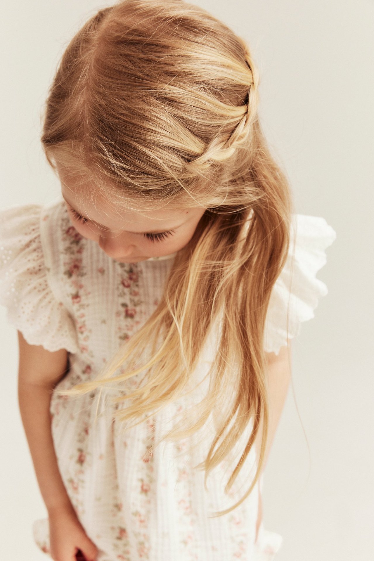 Högt vinklad närbild på ett barn i offwhite blommig muslintopp med broderade volangärmar.