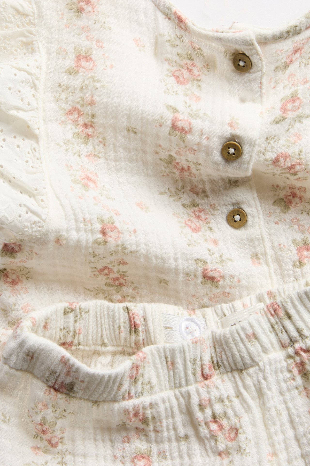 Zbliżenie na off-white kwiecisty muślinowy komplet dziecięcy: top peplum i szorty.