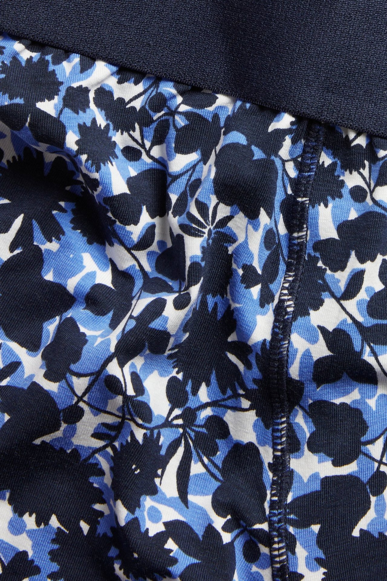 Zbliżenie na ciemnoniebieskie, niebieskie i białe, kwieciste bokserki jerseyowe z granatowym pasem elastycznym.