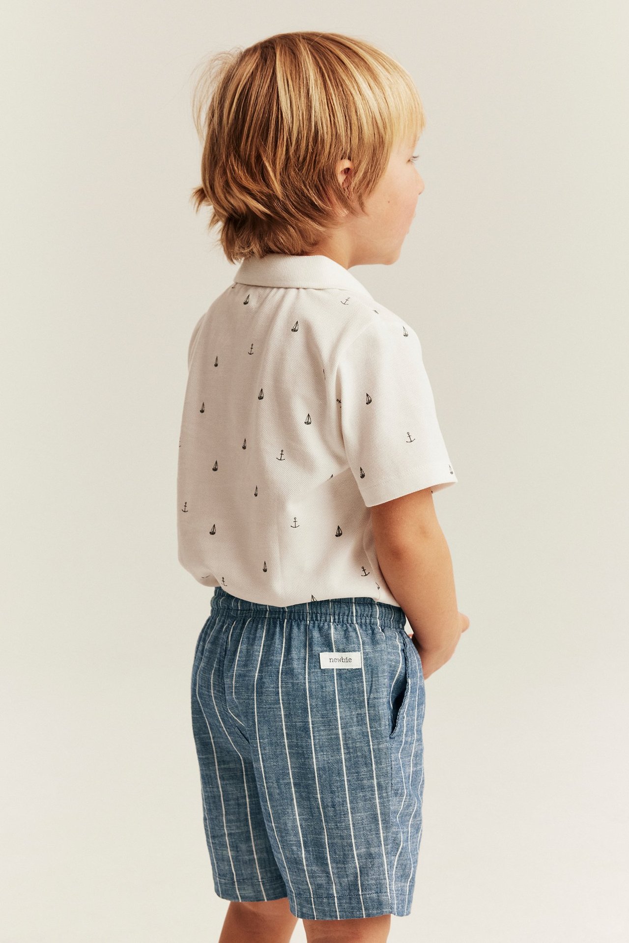Sidovy av ett barn som bär blårandiga vävda shorts med resårmidja och en vit mönstrad skjorta.