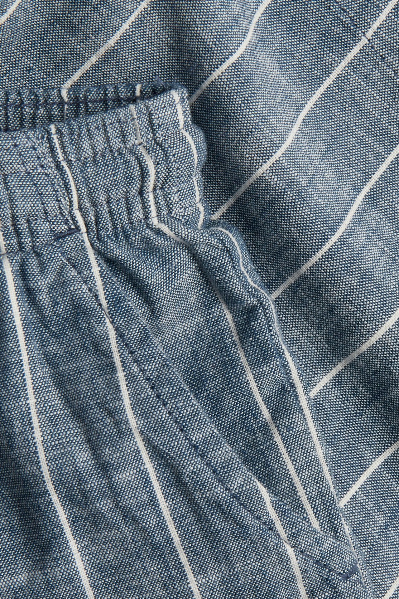 Nærbilde av blå og hvitstripete vevde bomullsshorts med elastisk linning og sidelomme.