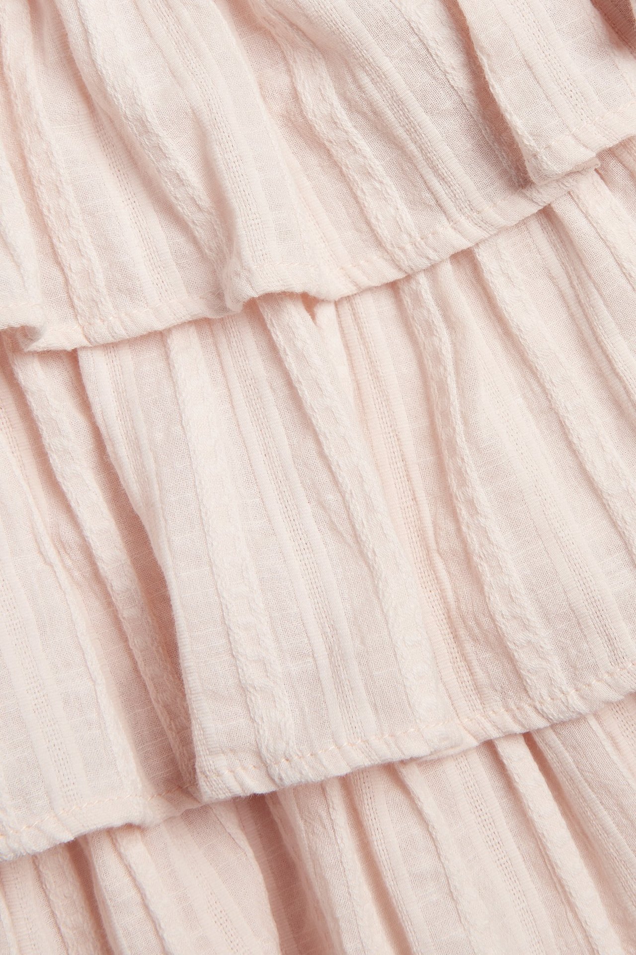 Nærbilde av en lys rosa vevd bluse med volanger og strukturert stripemønster.