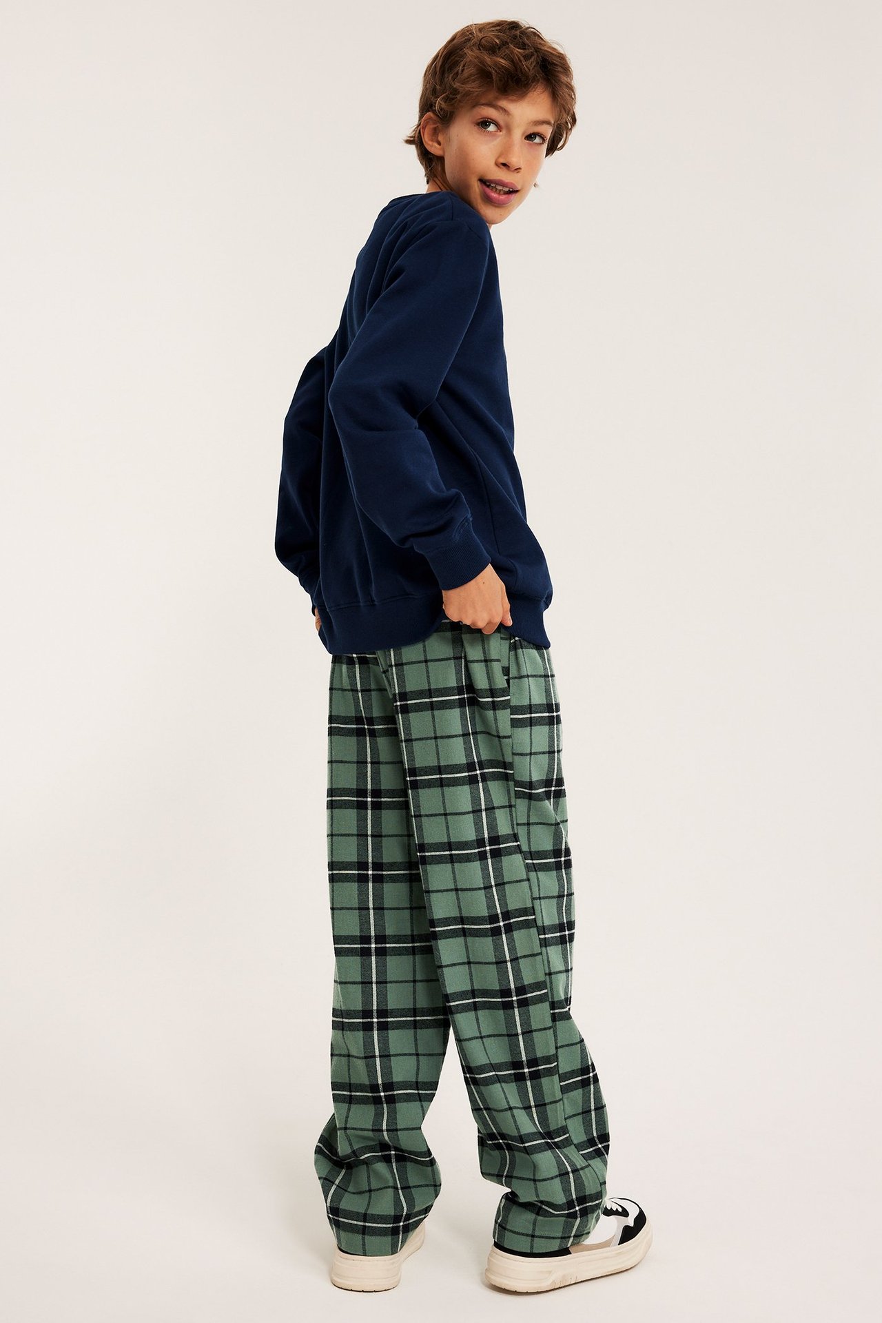 Sivukuva lapsesta vihreissä ruudullisissa flanellipyjamahousuissa, tummansinisessä collegepaidassa ja lenkkareissa.