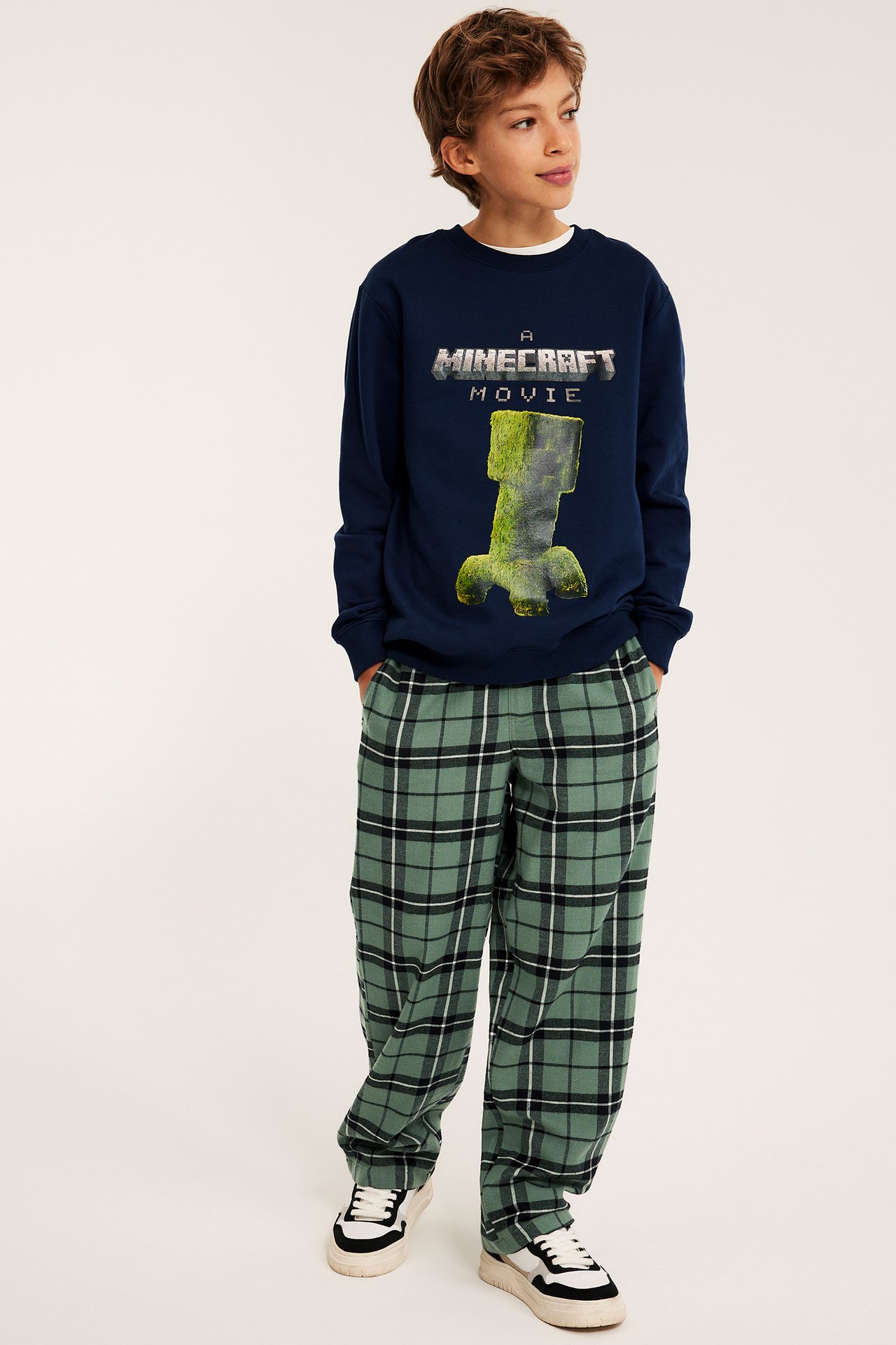 Etukuvassa lapsi yllään vihreät ruudulliset flanellipyjamahousut ja laivastonsininen Minecraft-collegepaita.