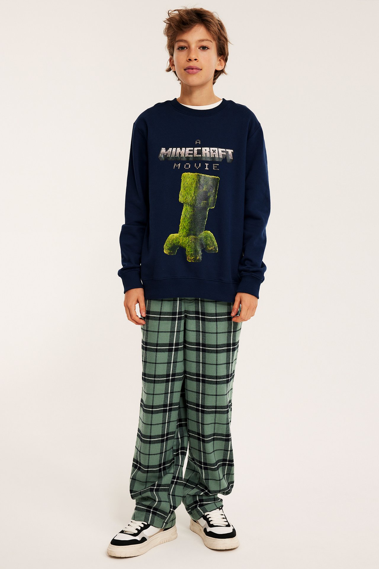 Edestä, lapsi yllään vihreät ruudulliset flanellipyjamahousut ja tummansininen Minecraft-collegepaita.