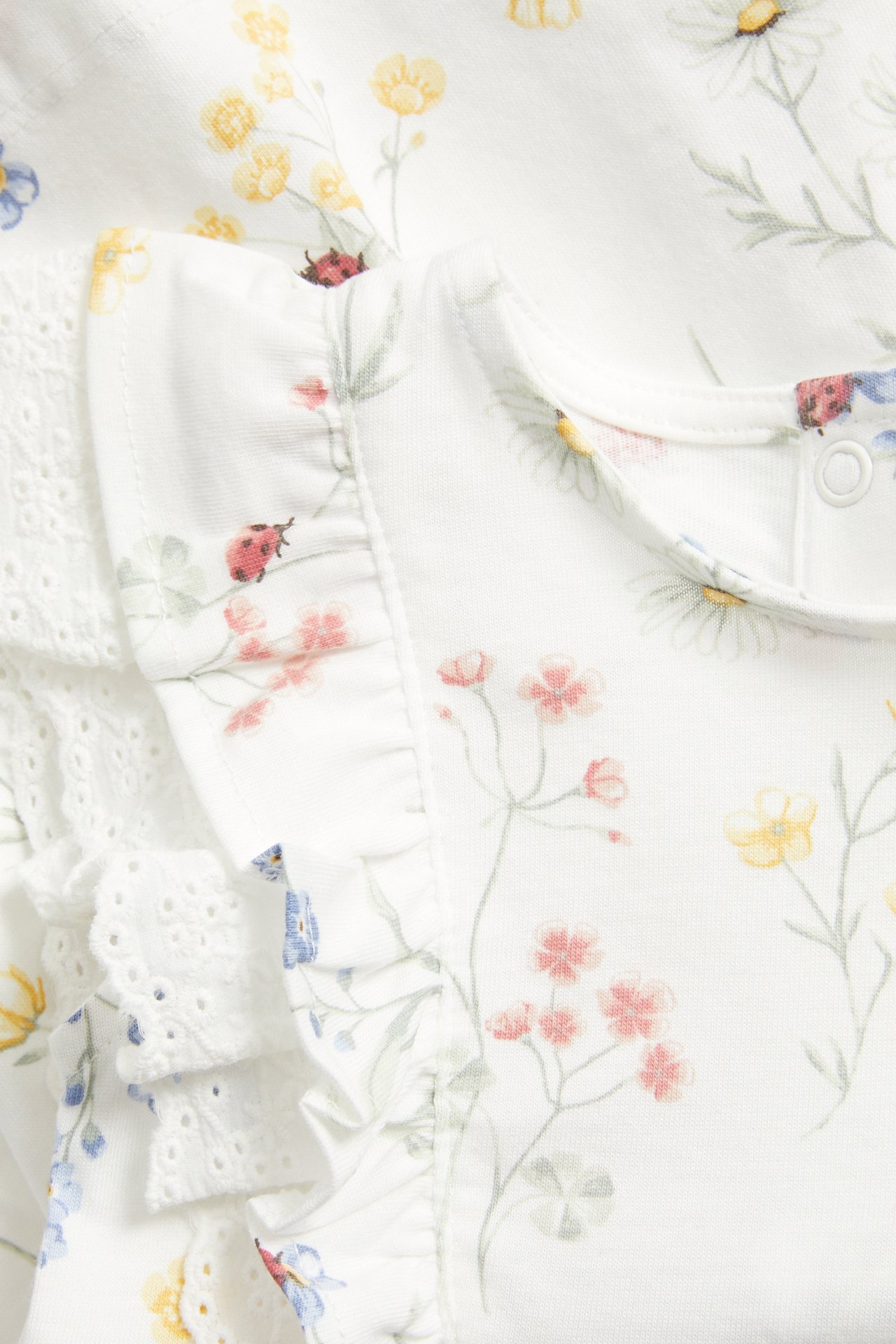 Nærbilde, forfra, av en offwhite bomullsjerseykjole med blomstermønster, volanger og blondedetaljer.