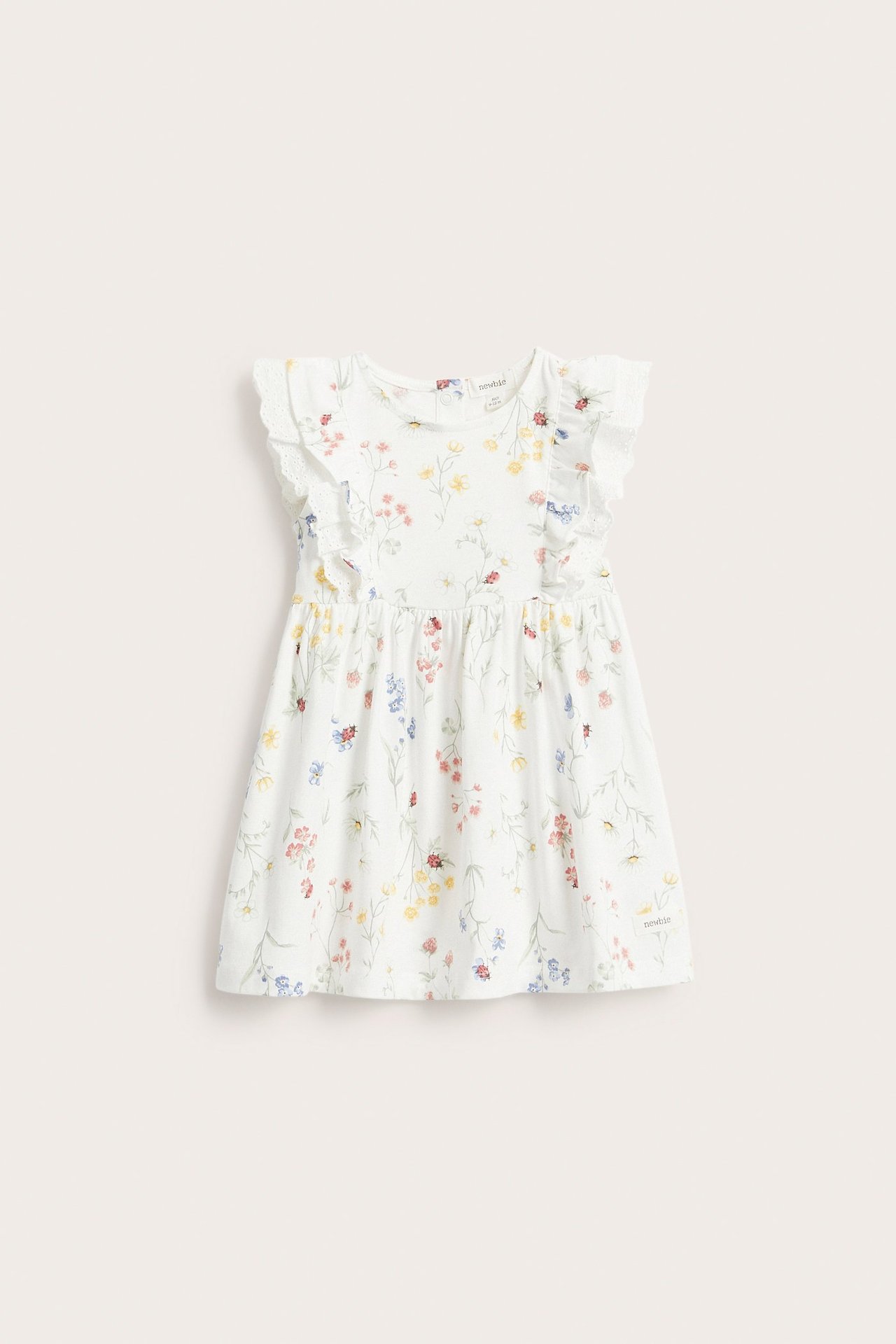 Frontvy av en offwhite jerseyklänning för barn med volanger, spetsdetaljer och färgglatt blommigt mönster.