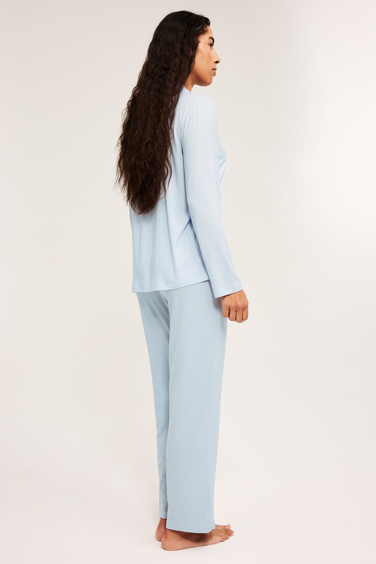 Widok z boku kobiety w jasnoniebieskiej piżamie z dżerseju lyocell, z luźną koszulą i szerokimi spodniami.