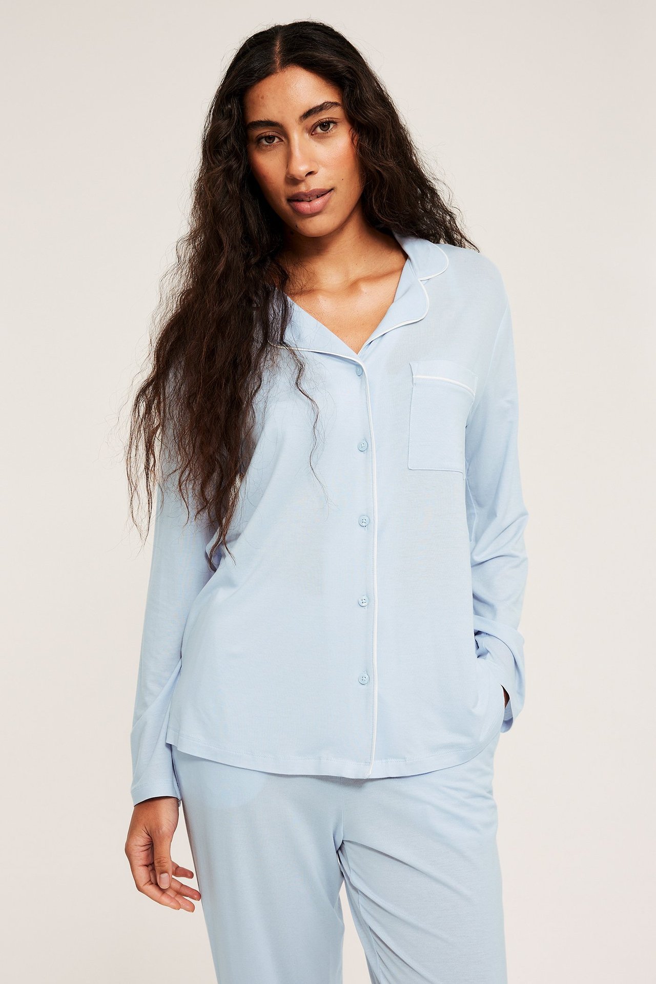 Widok z przodu: kobieta w jasnoniebieskiej piżamie lyocell z białą lamówką na koszuli i spodniach.