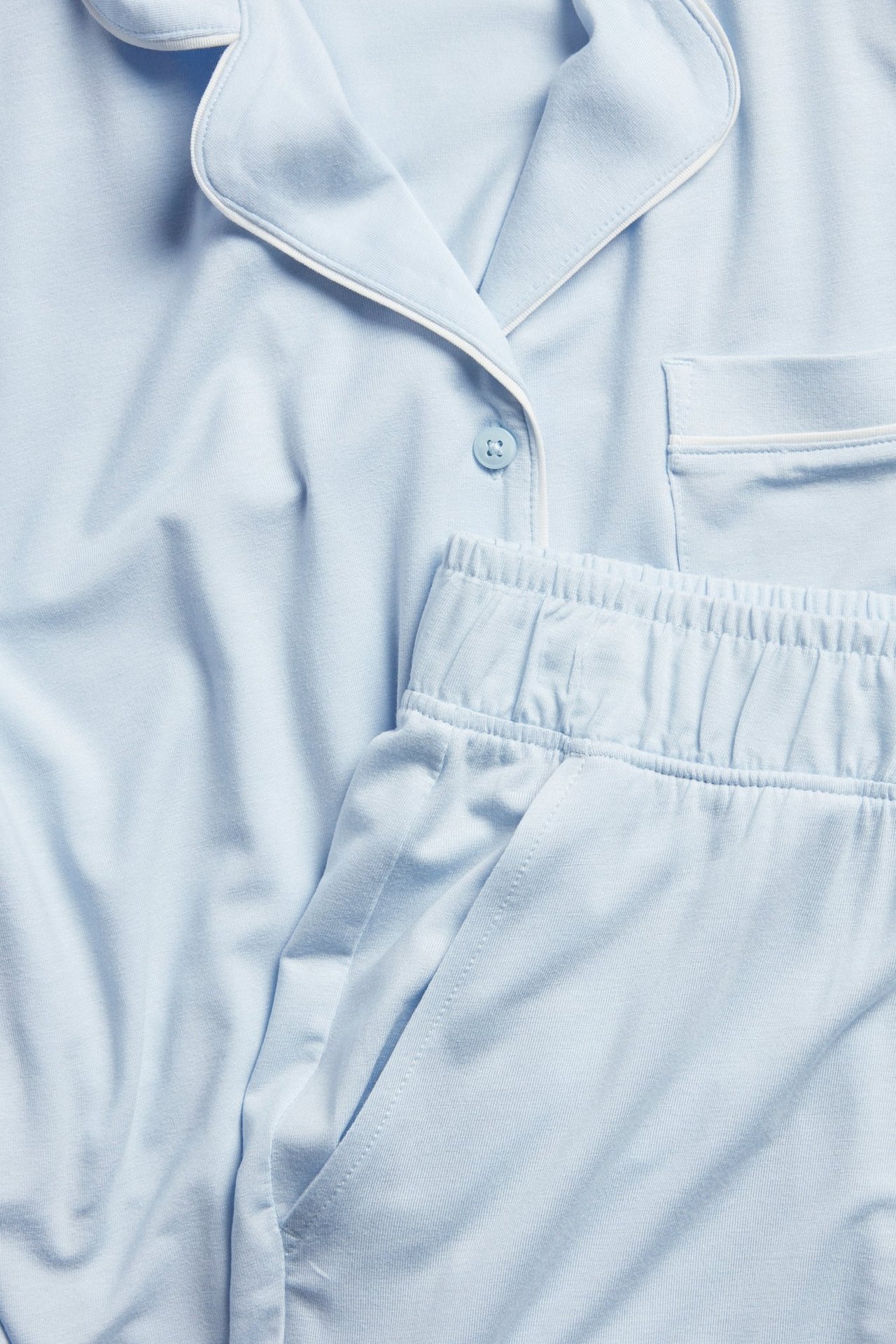 Zbliżenie na jasnoniebieską piżamę lyocell: koszula zapinana na guziki z kieszenią, spodnie z gumką i kieszenią.