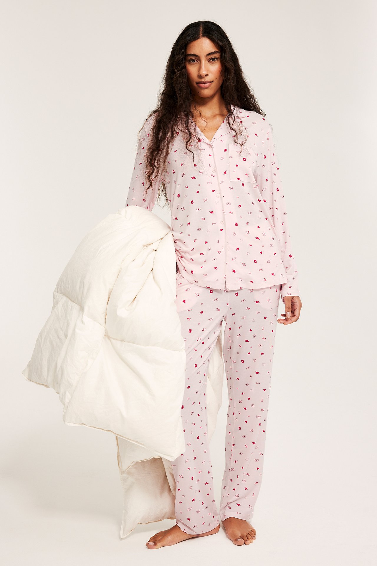 Widok z przodu: kobieta w jasnoróżowej, wzorzystej piżamie z lyocellu, trzyma białą kołdrę.