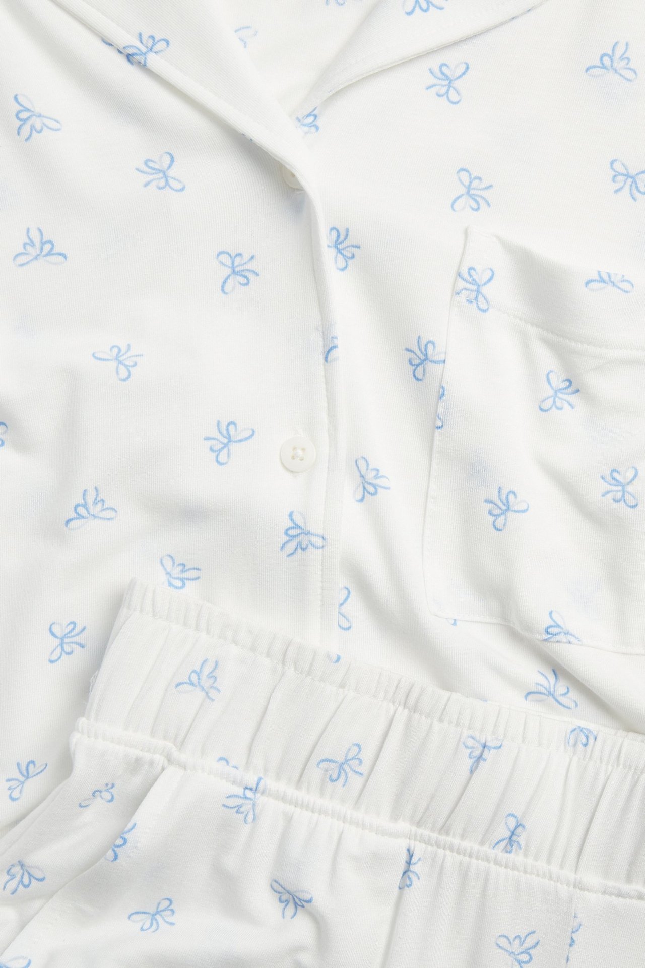 Nærbilde av offwhite lyocellpyjamas med blått sløyfemønster, knappet topp og bukser med elastisk linning.