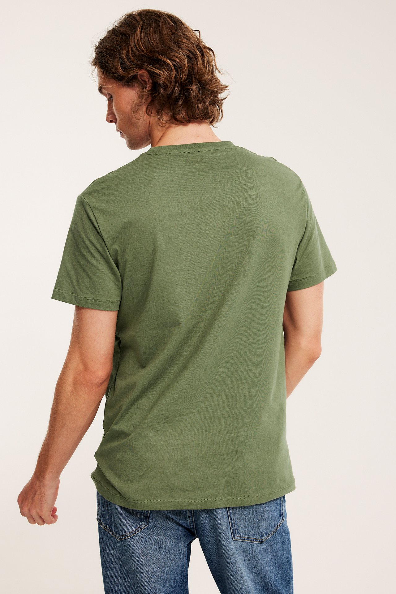 Mann sett bakfra, iført en ensfarget khaki grønn rundhalset bomulls t-skjorte og blå jeans.