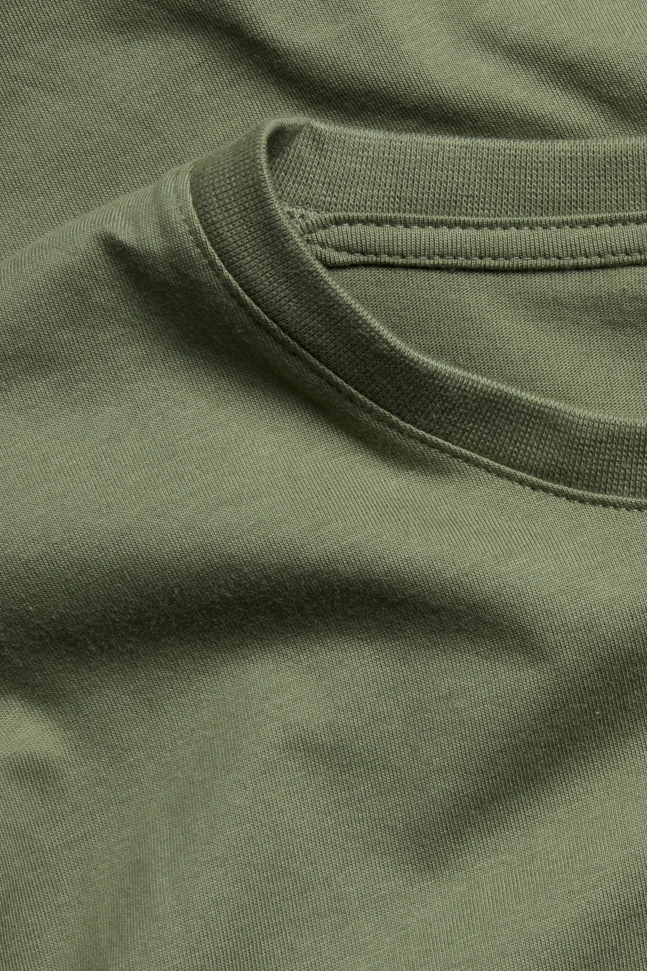 Nærbilde av en khakigrønn, rundhalset bomulls-t-skjorte, viser ribbet halslinning og stofftekstur.