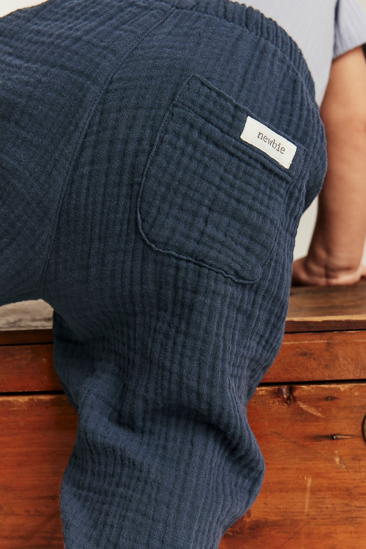 Lähikuva takaa vauvasta yllään tummansiniset puuvillamusliinikudotut housut, joissa takatasku.