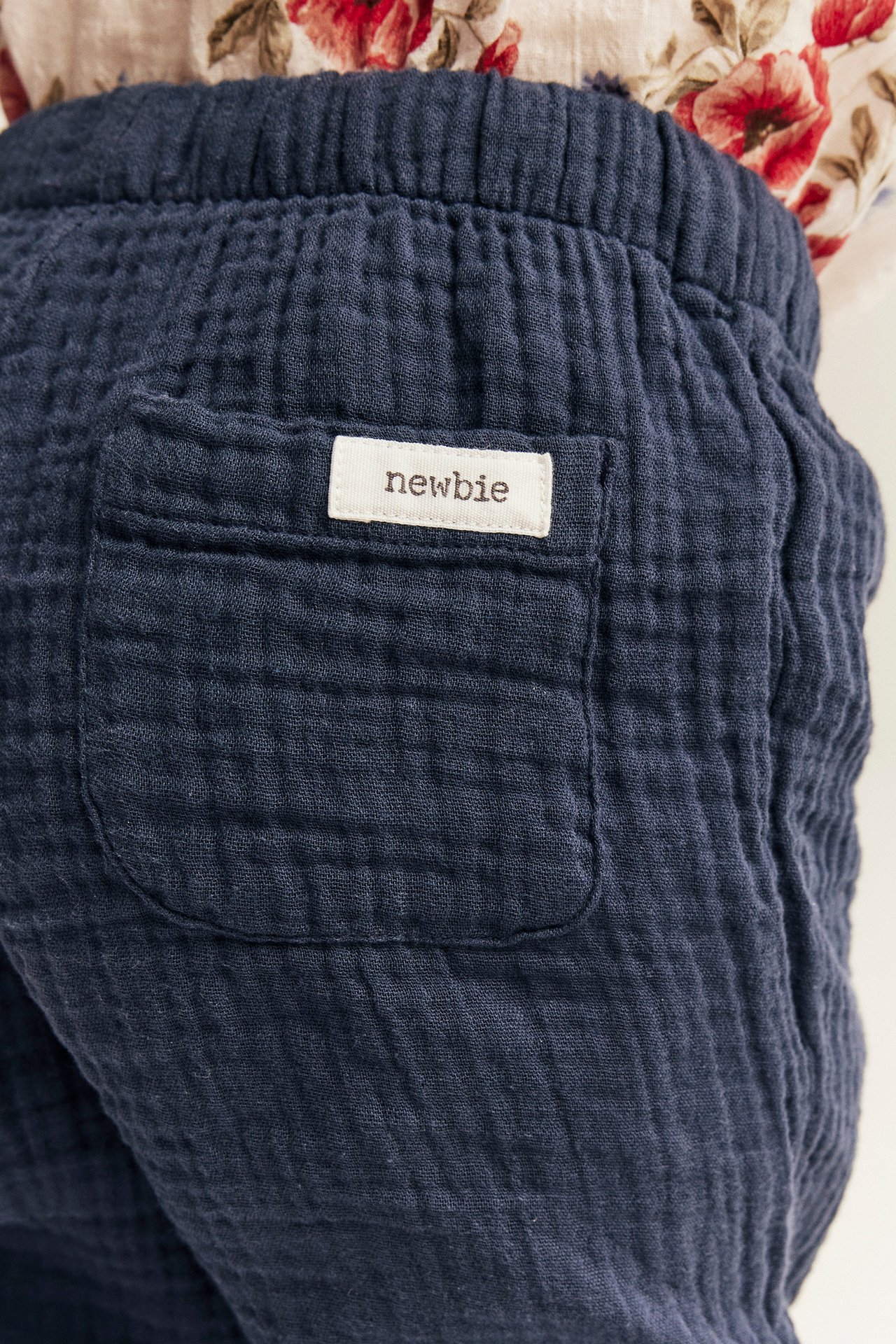 Närbild bakifrån: mörkblå muslinbyxor för barn med resårmidja och bakficka, burna med en blommig topp.