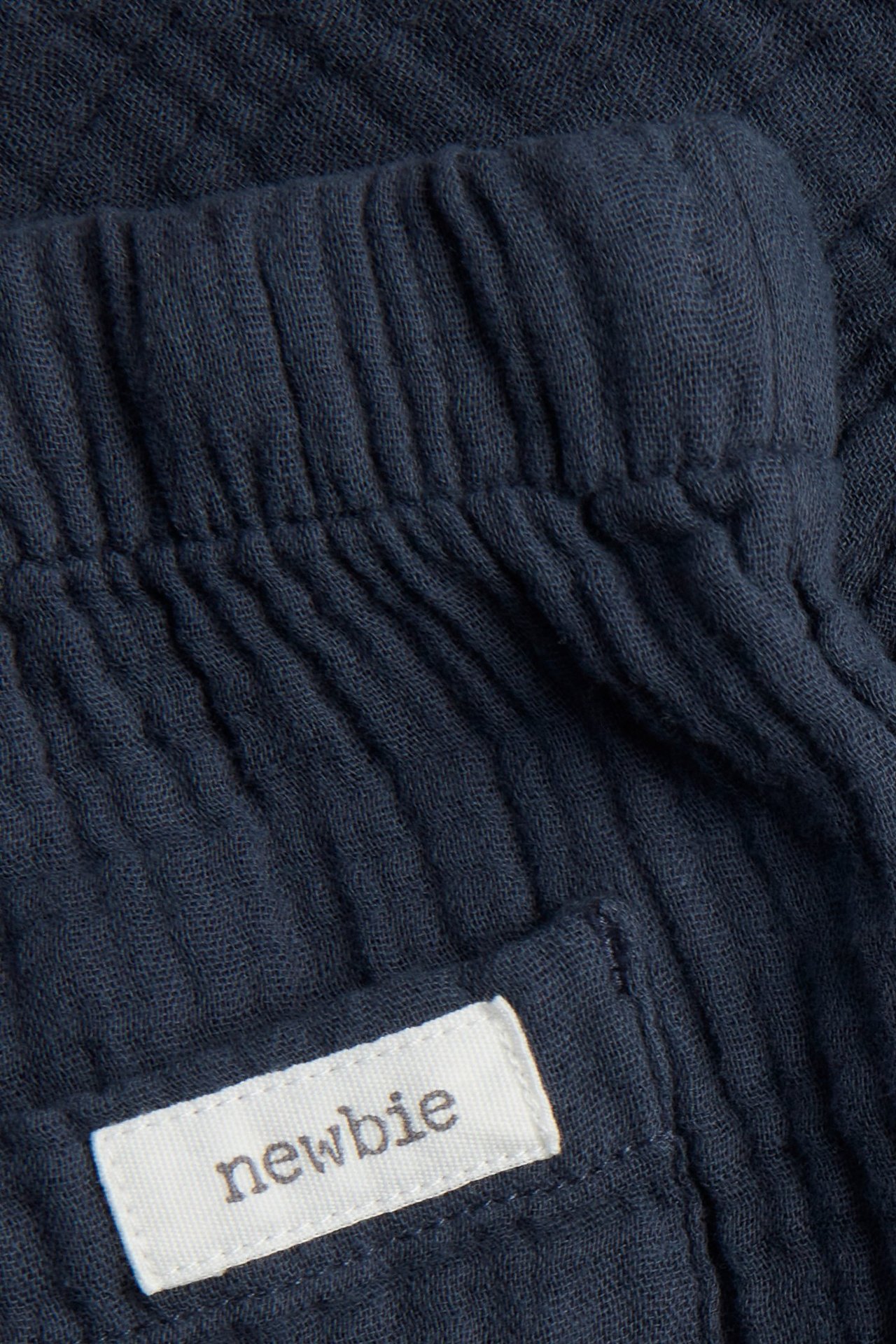 Lähikuva tummansinisistä puuvillamusliinihousuista, joustava vyötärö, 'newbie'-merkki takataskussa.