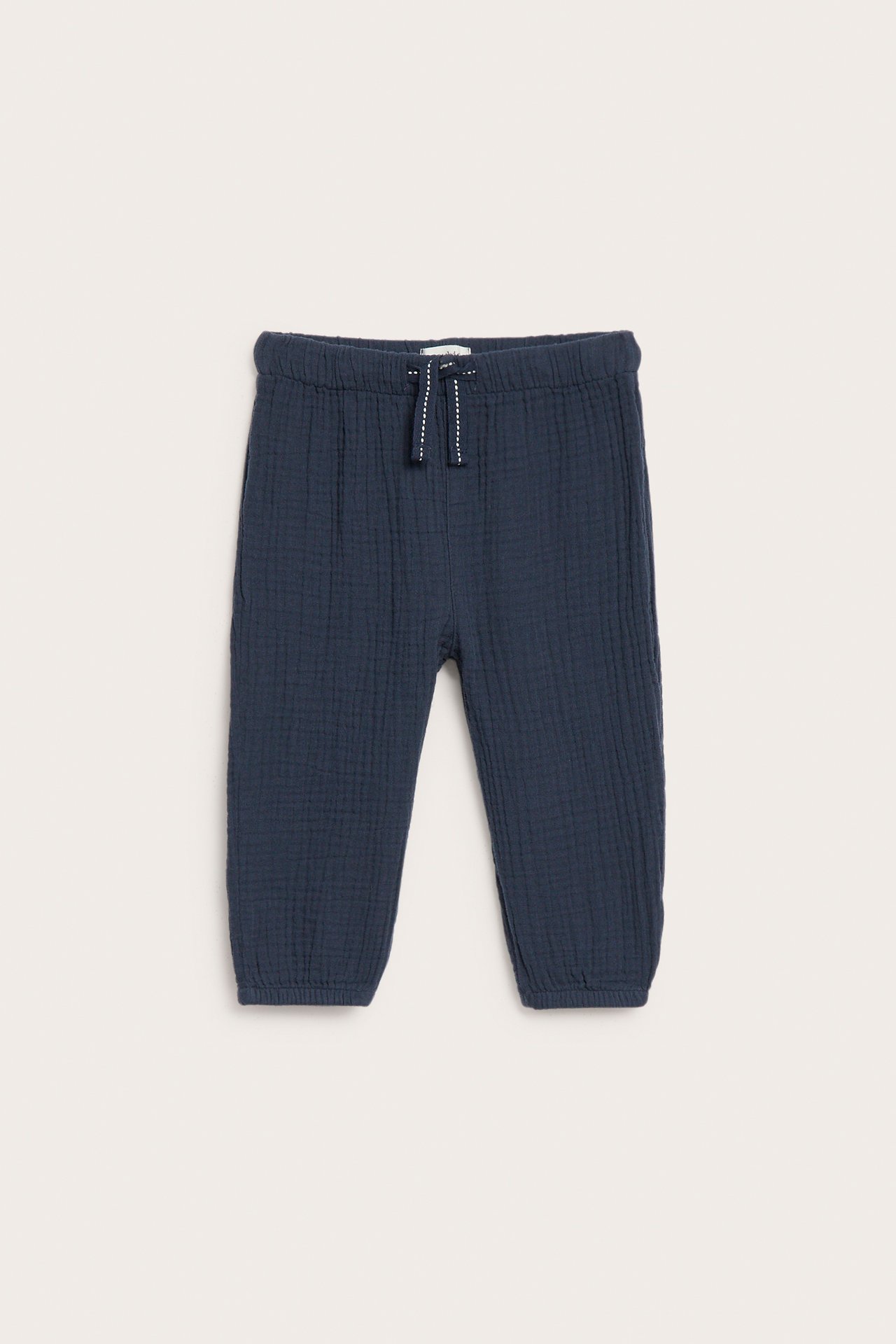 Edestä: Tummansiniset kudotut lastenhousut puuvillamusliinista, joustovyötäröllä, valkoisella kiristysnyörillä, joustavat lahkeet.