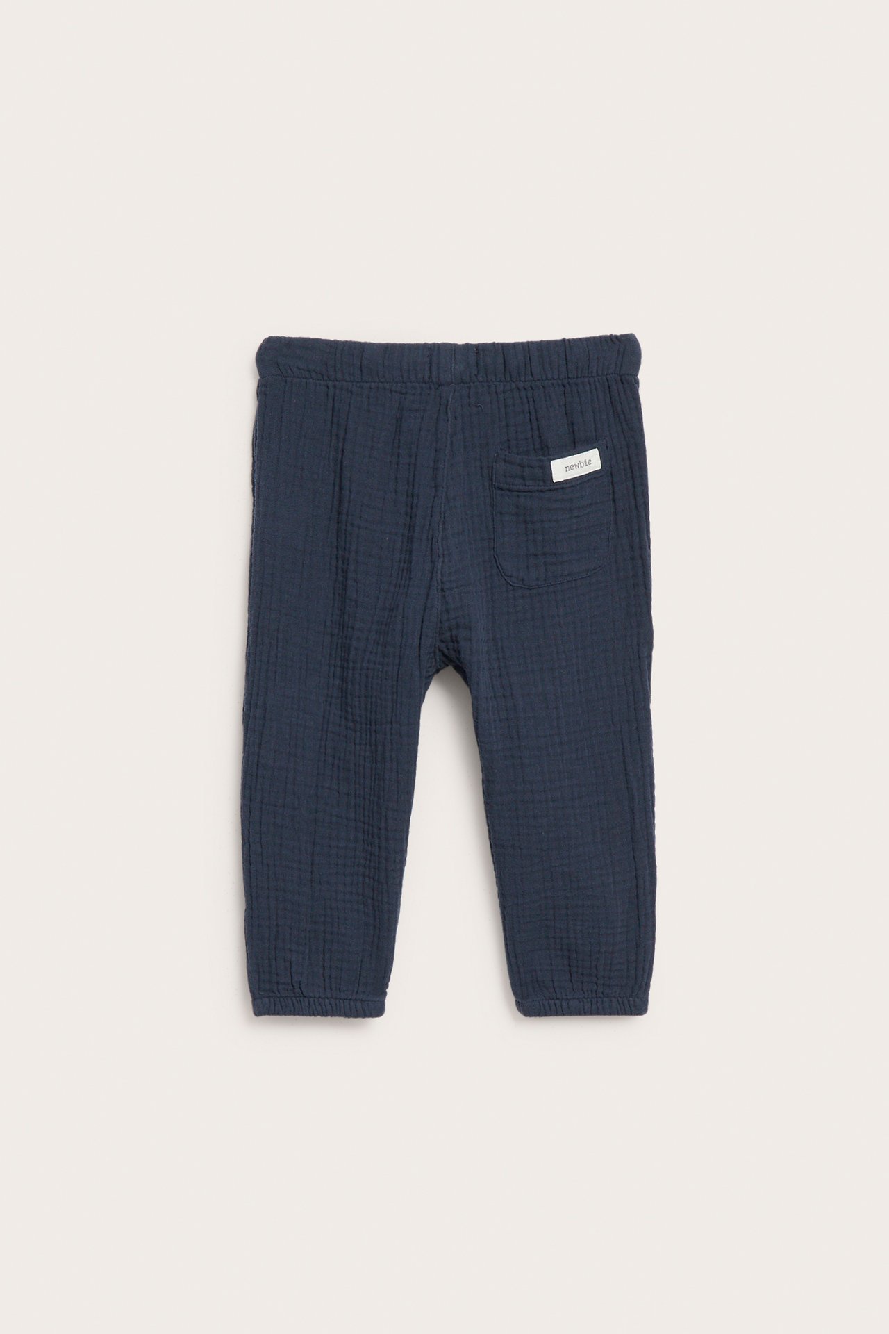 Bakifrån mörkblå vävda babybyxor i bomullsmuslin med resår i midjan och en bakficka.