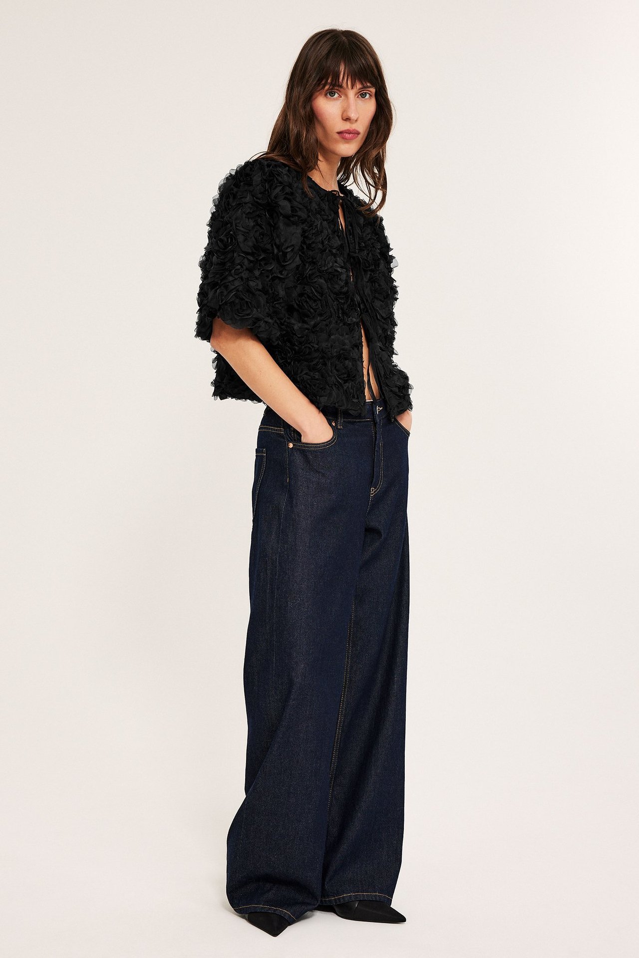 Svart puffärmbluse med knyting, åpen foran, over mørke jeans.