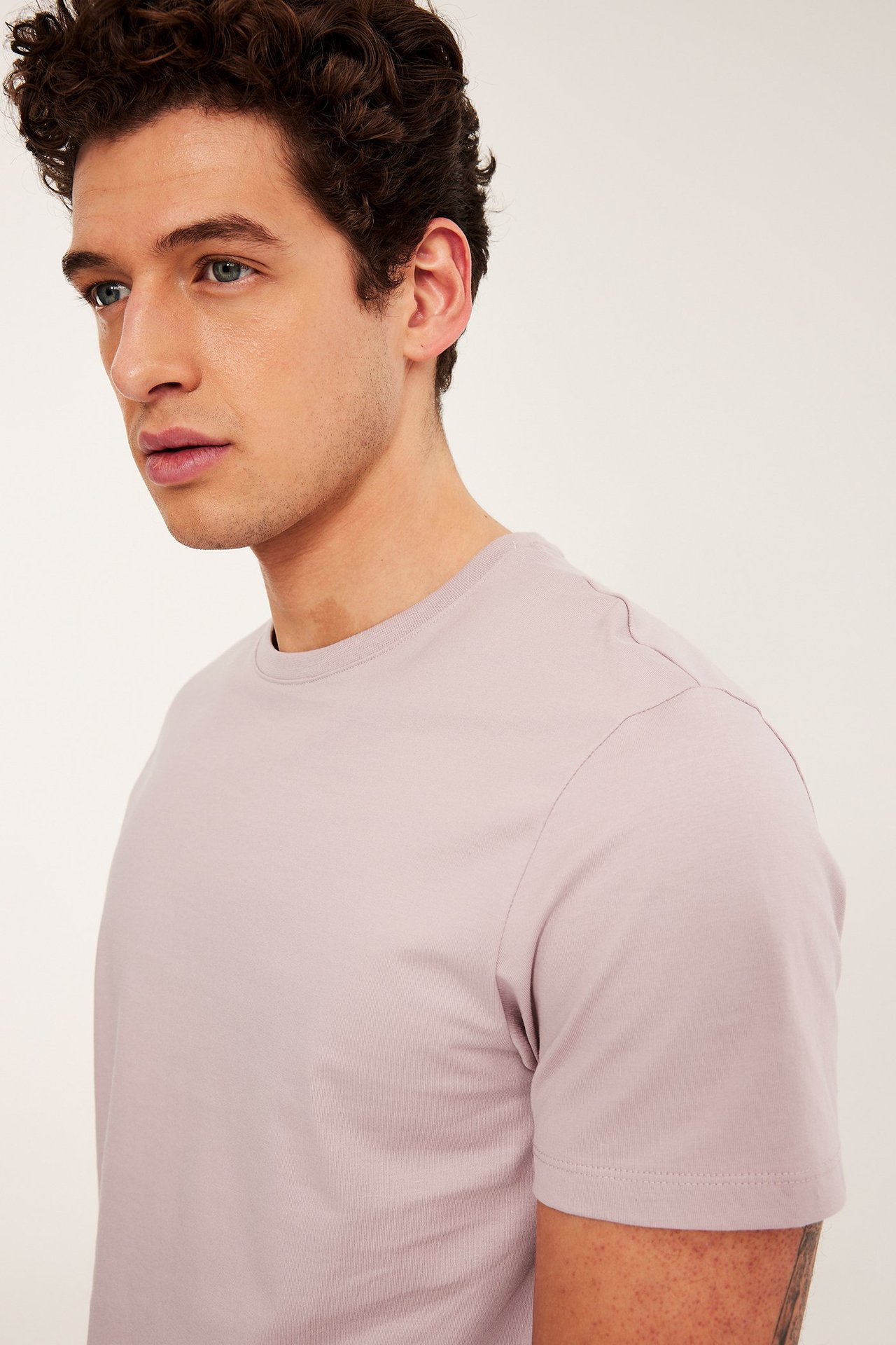 Närbild, sidovy av en man i en enfärgad ljusrosa rundhalsad kortärmad t-shirt.