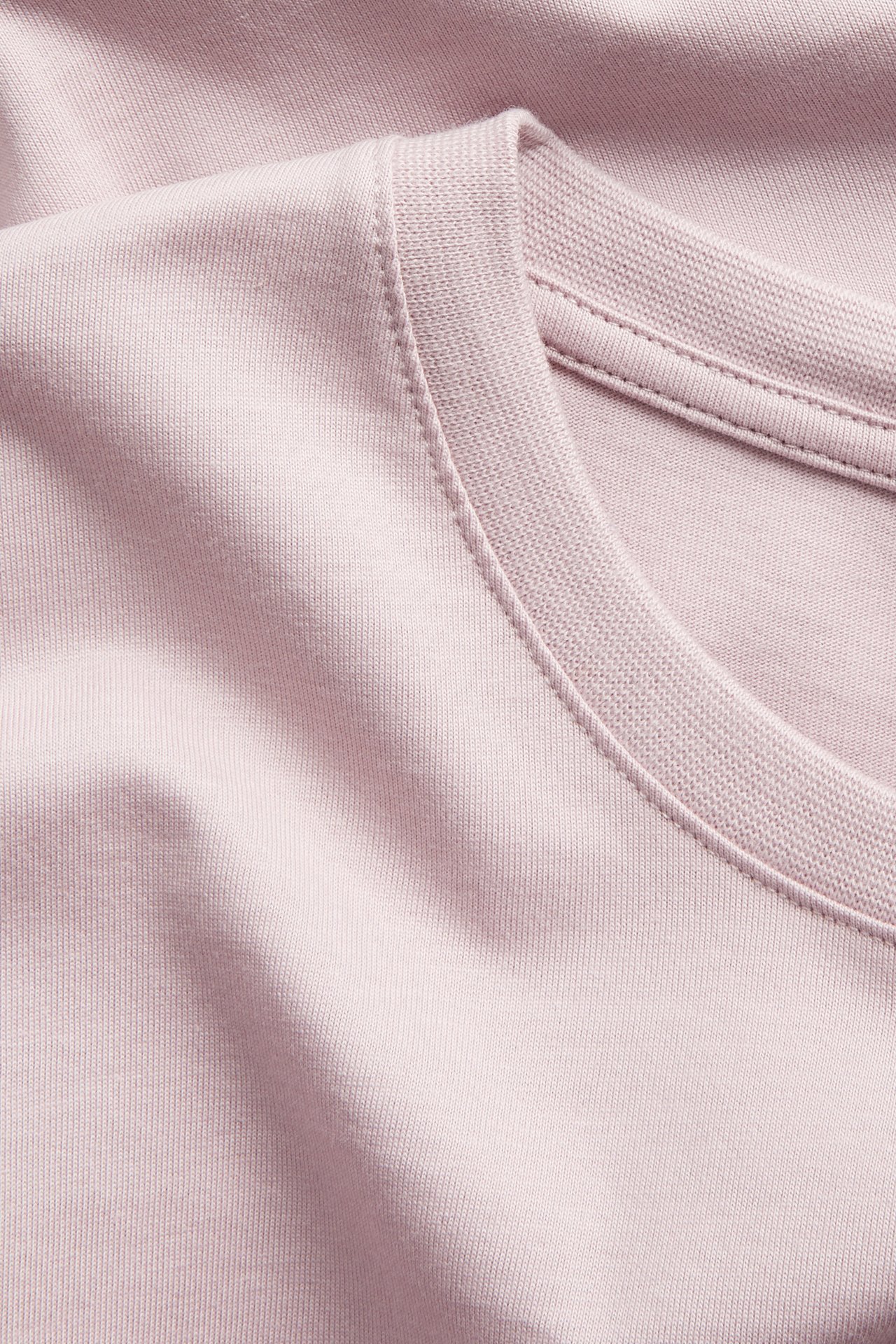 Nærbilde av en ensfarget lyserosa rundhalset bomulls-T-skjorte for menn.