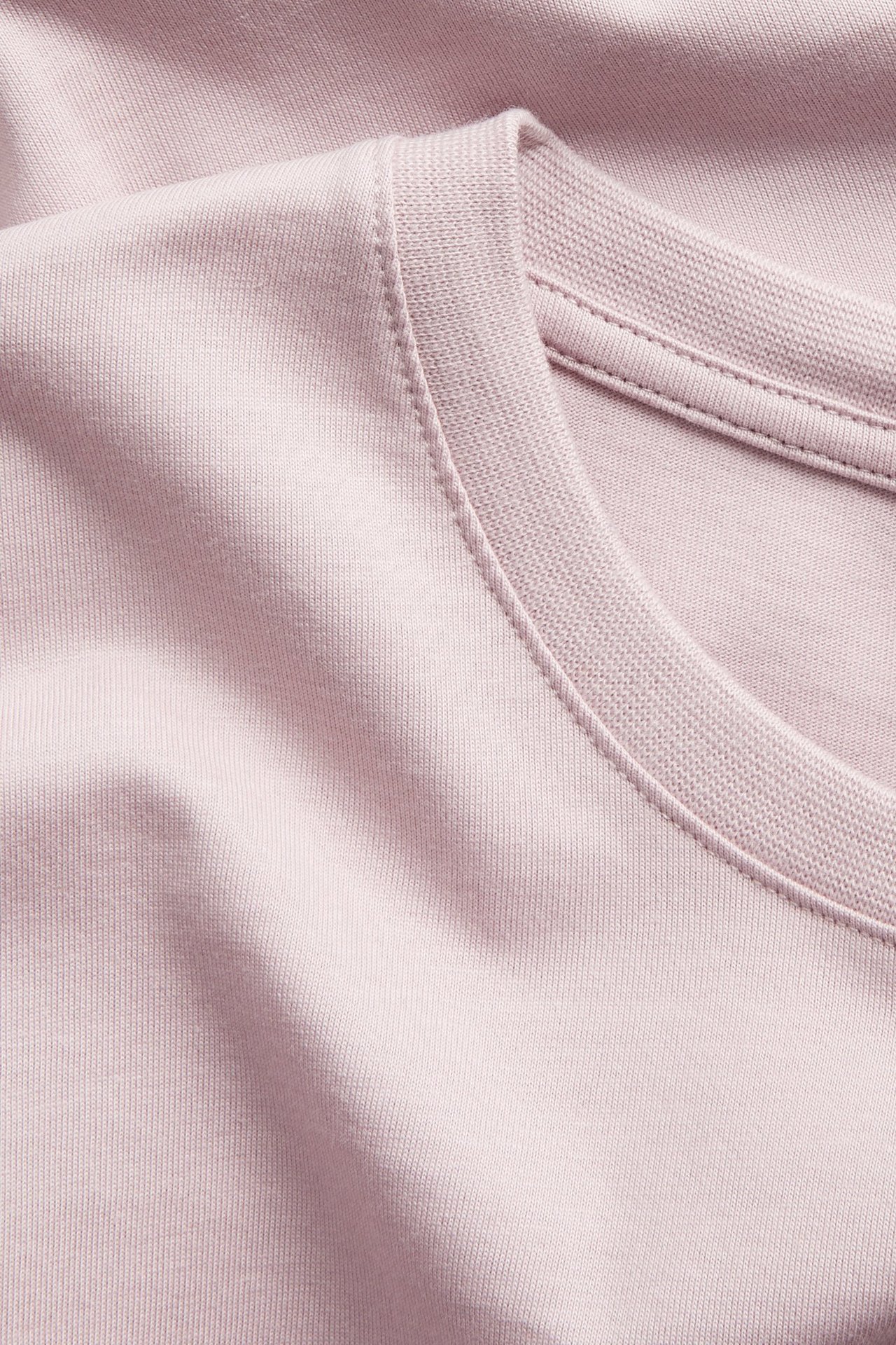 Nærbilde av en ensfarget lyserosa rundhalset bomulls-T-skjorte for menn.