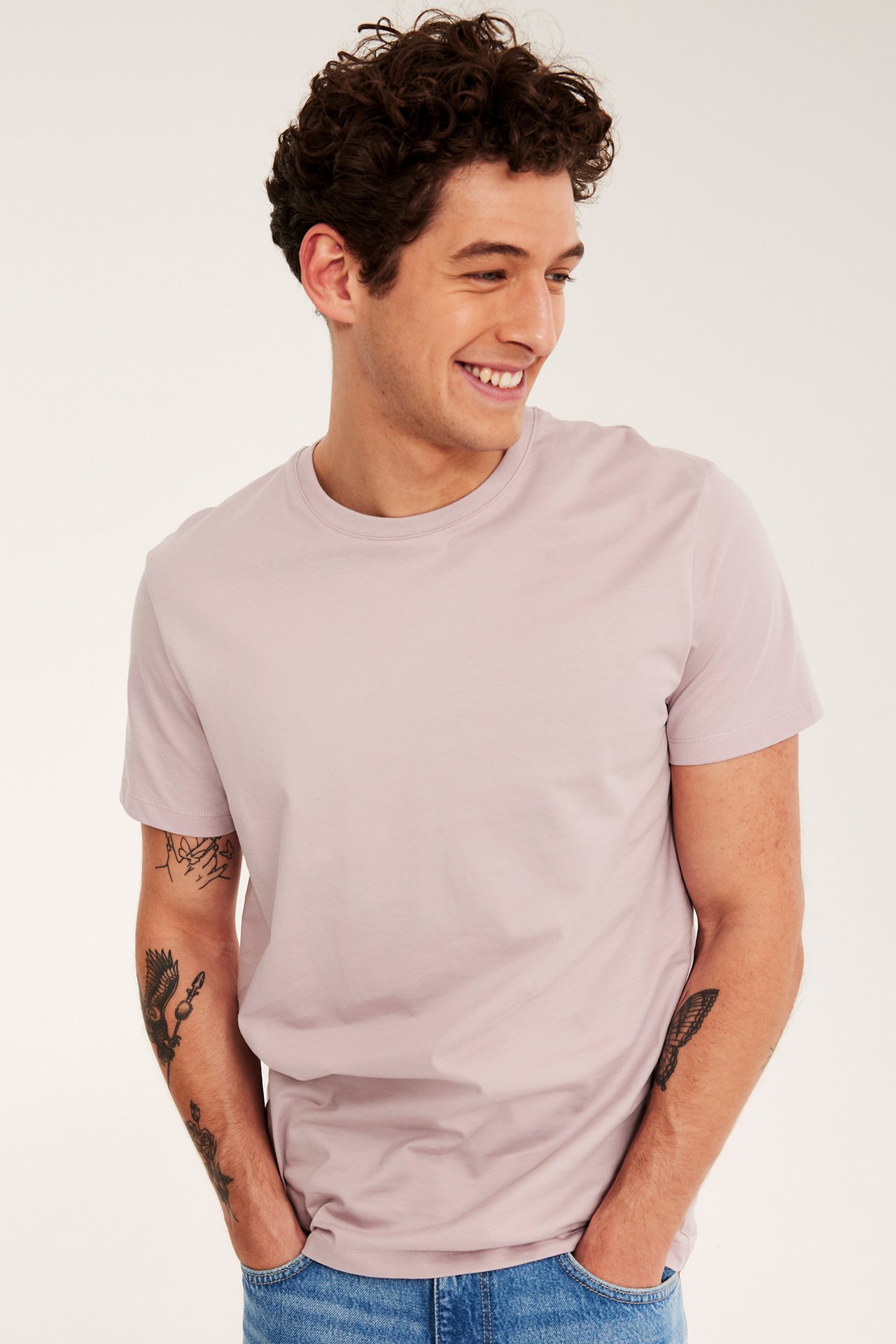 Frontvy av en man i ljusrosa rundhalsad bomulls-t-shirt och blå jeans.